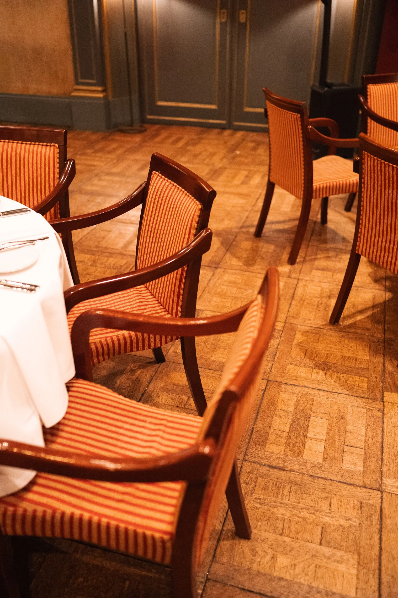 Empty restaurant with round table, orange striped chairs, and closed double doors in the background.