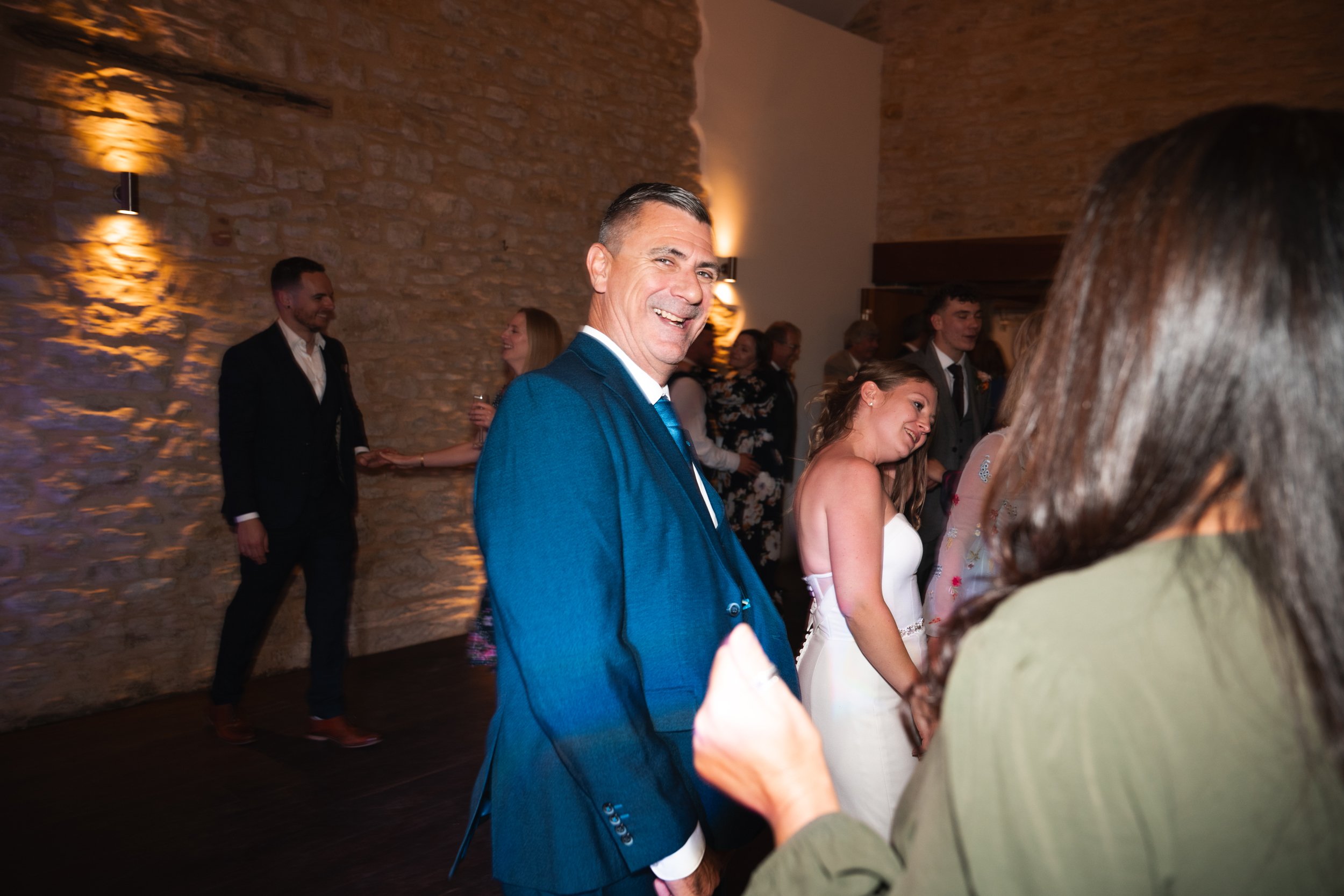 People dancing at a wedding reception in a rustic indoor venue with brick walls and warm lighting.