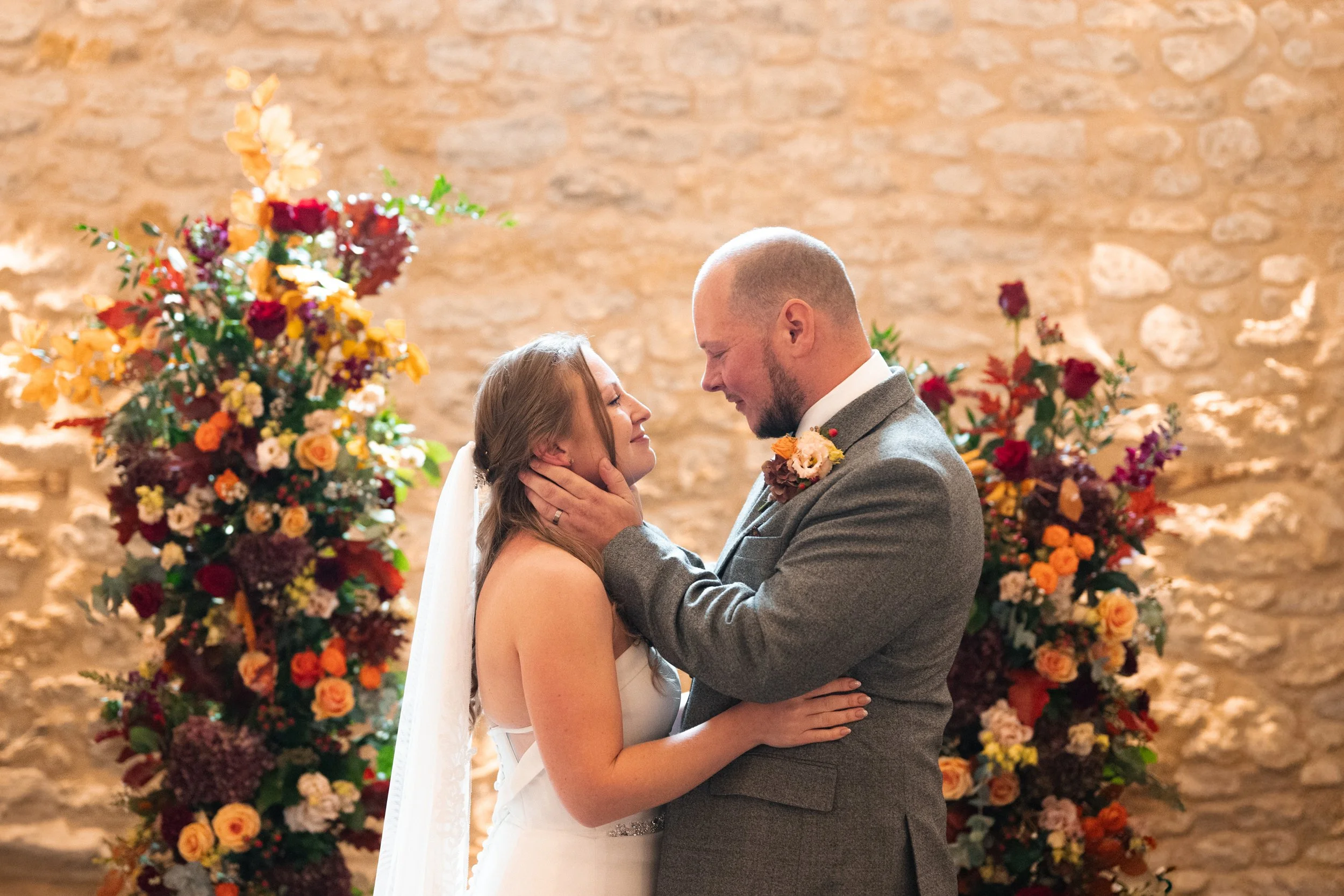 A bride and groom share an intimate moment during their wedding ceremony, with colorful floral arrangements in the background.