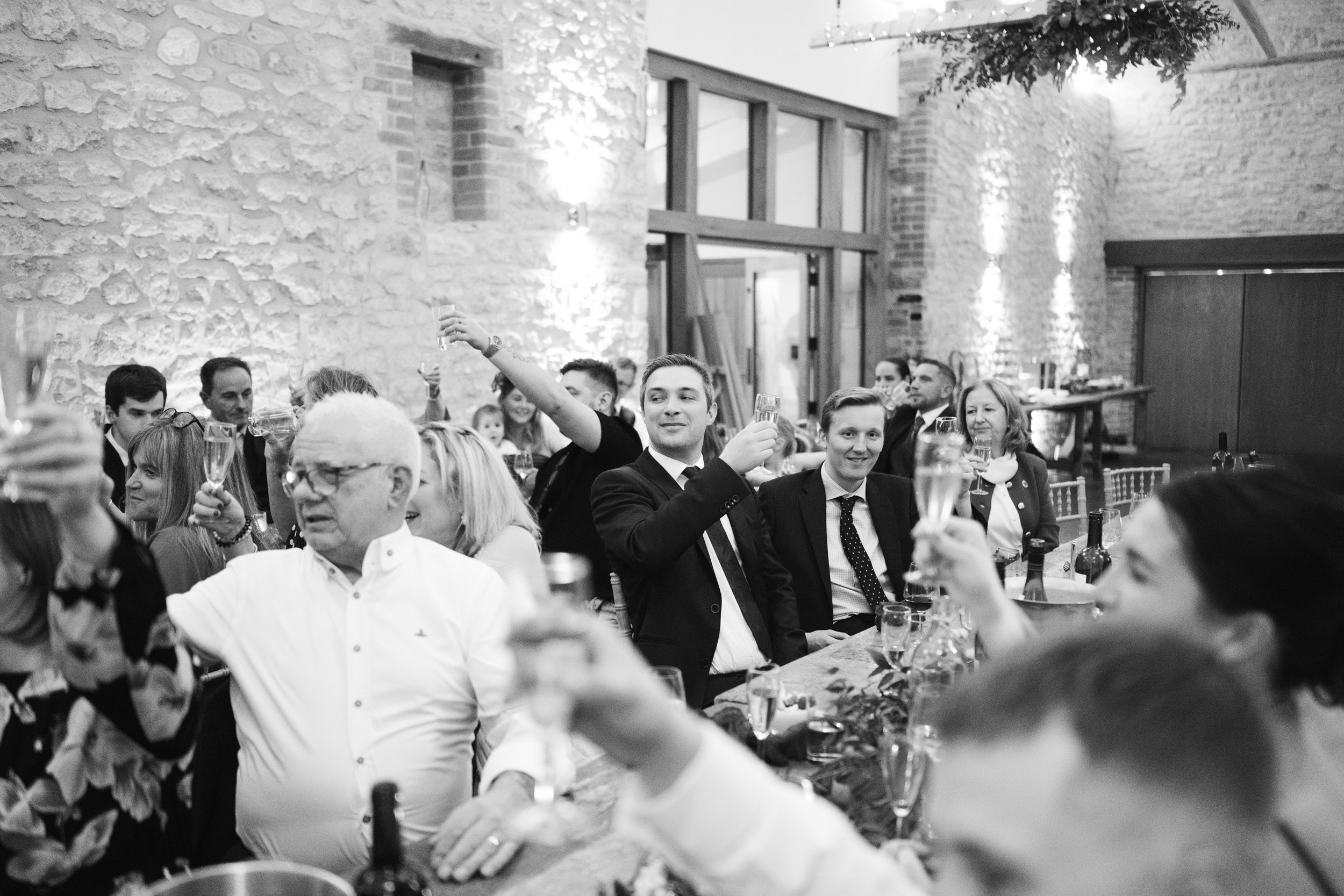 People celebrating at a party or wedding reception, toasting with champagne glasses in a rustic venue with stone walls and warm lighting.