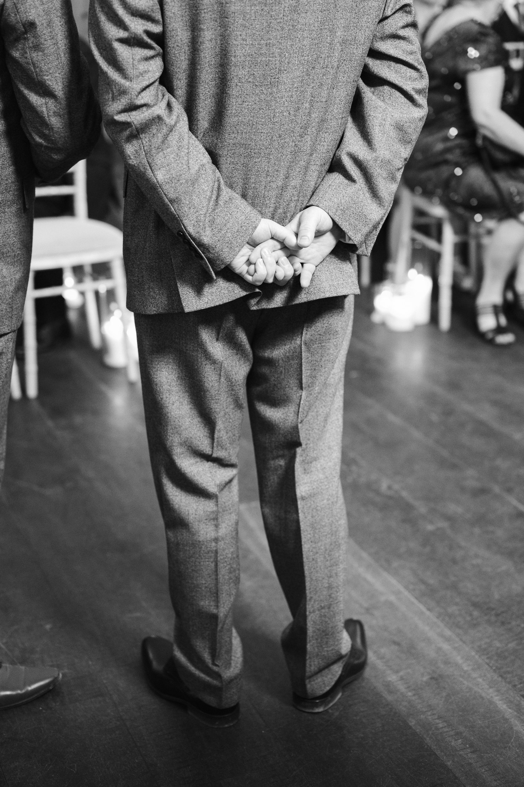 Back view of a man in a suit with hands clasped behind his back at a formal event.