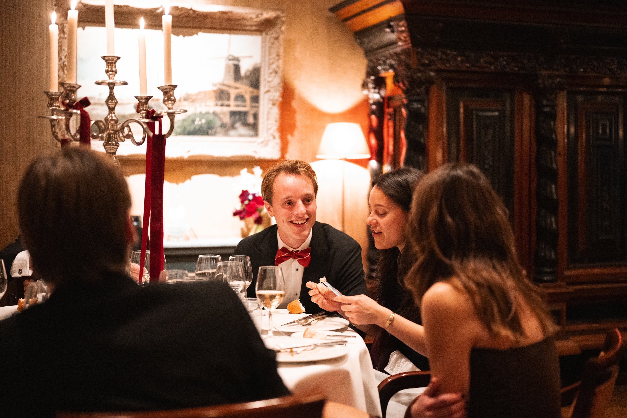 People sitting around a dinner table, smiling and talking, with lit candles on a candelabrum, in a warmly decorated restaurant.