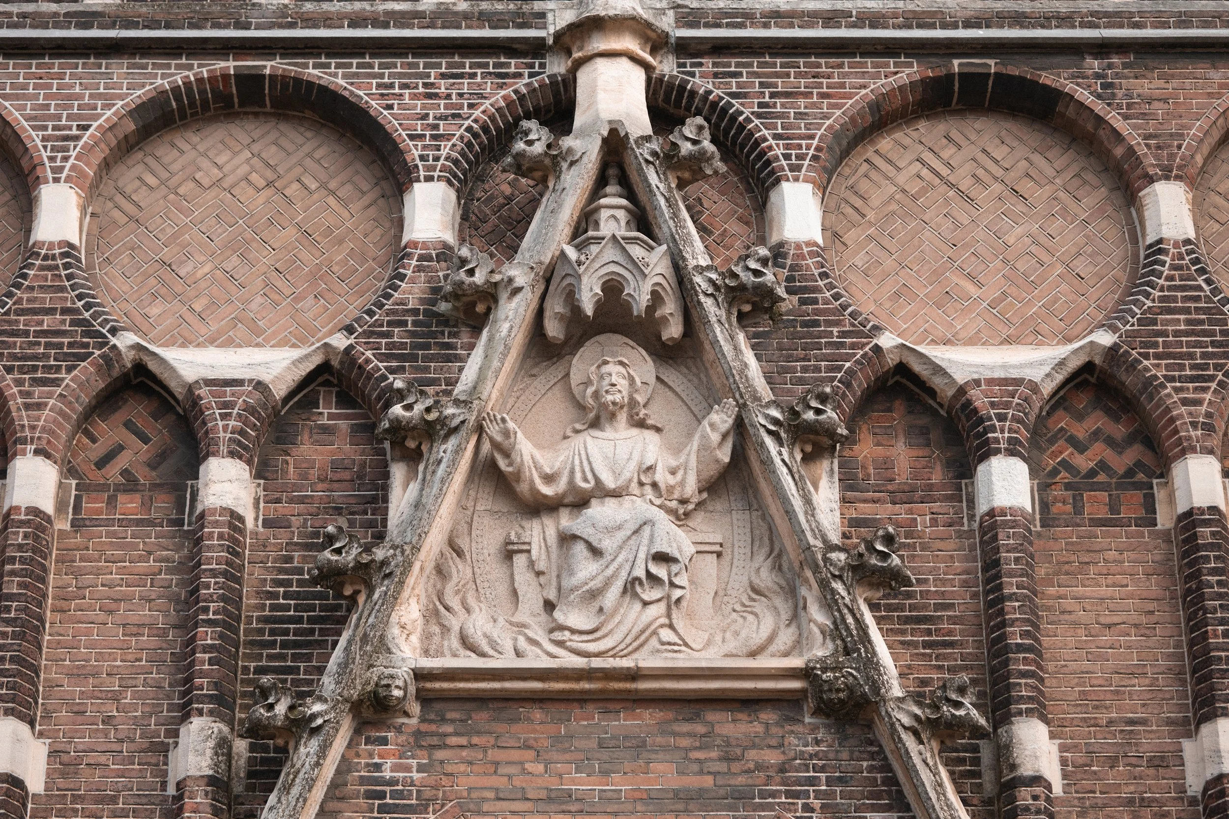 Religious stone carving of Jesus Christ with open arms in a triangular frame on a brick church wall.