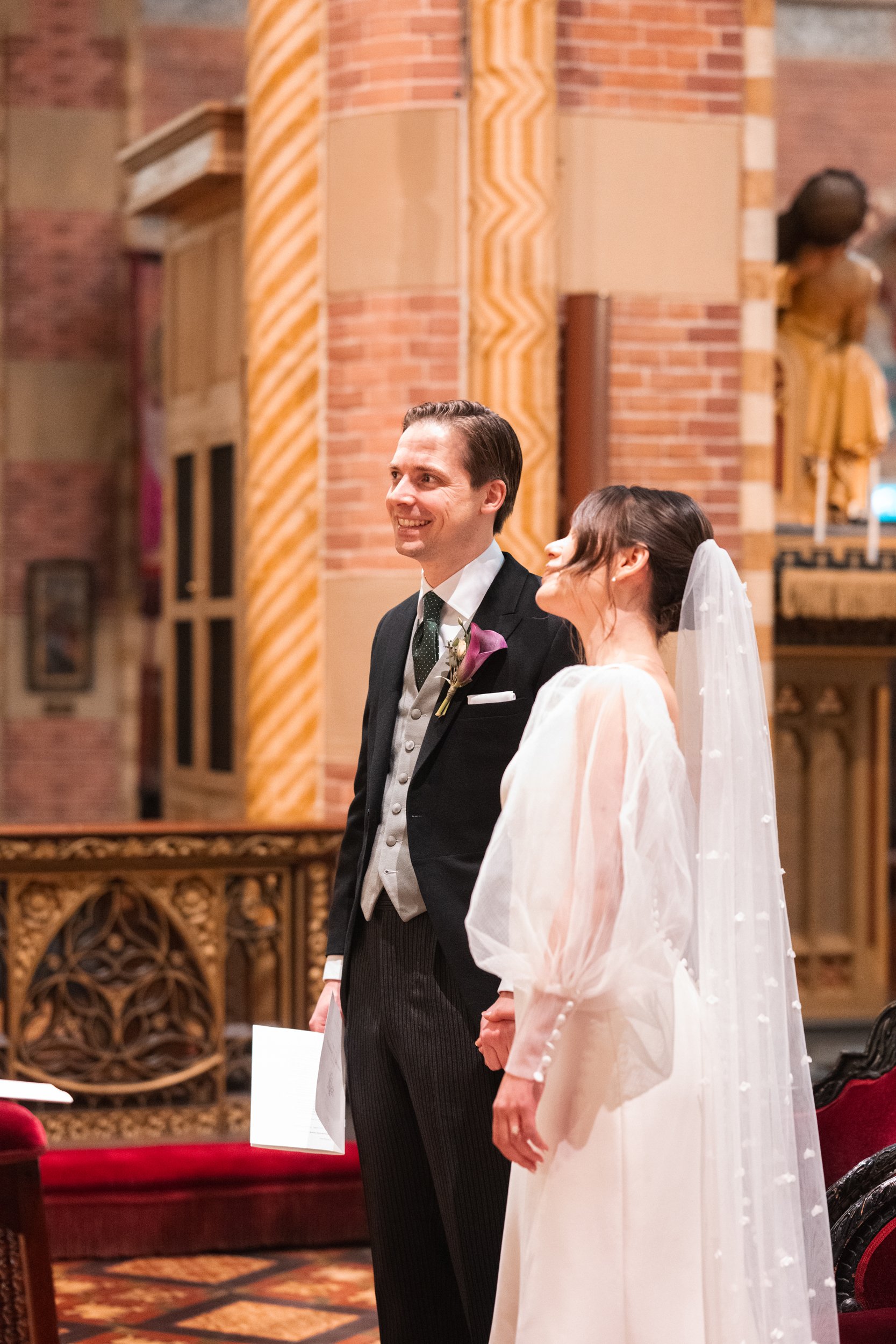 A groom and bride standing hand in hand during a wedding ceremony inside a church.