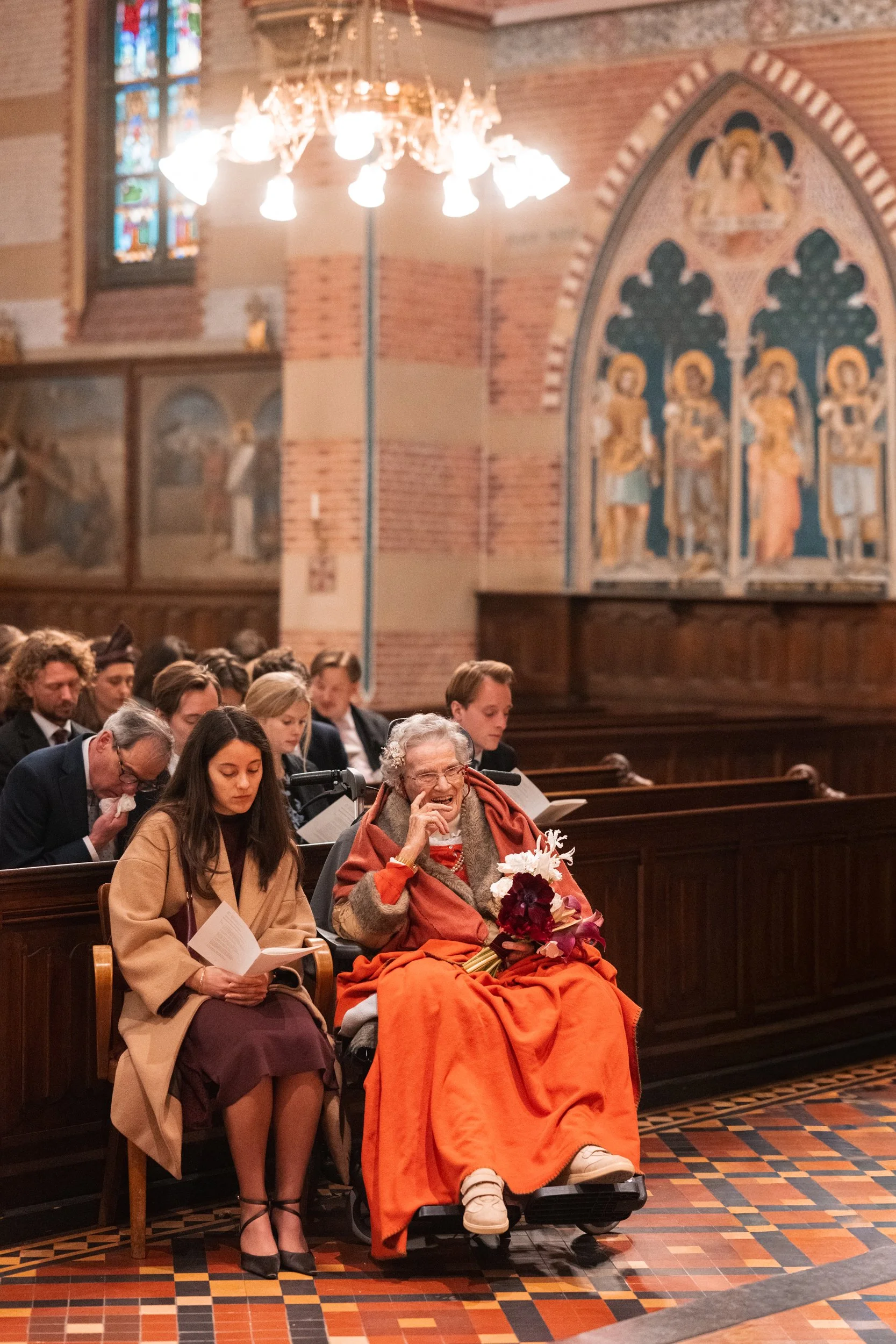 A diverse group of people seated in a church, participating in a religious service or ceremony, with stained glass windows and religious artwork in the background.