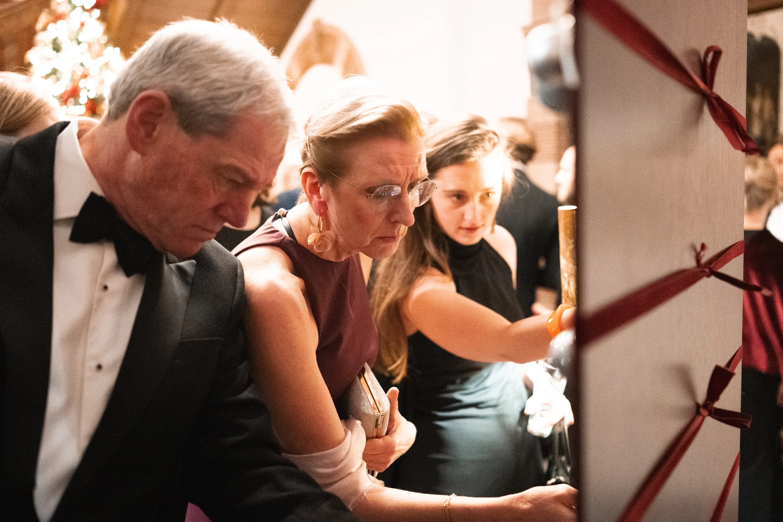 People at a Christmas party playing a game or signing a card, with a Christmas tree in the background.