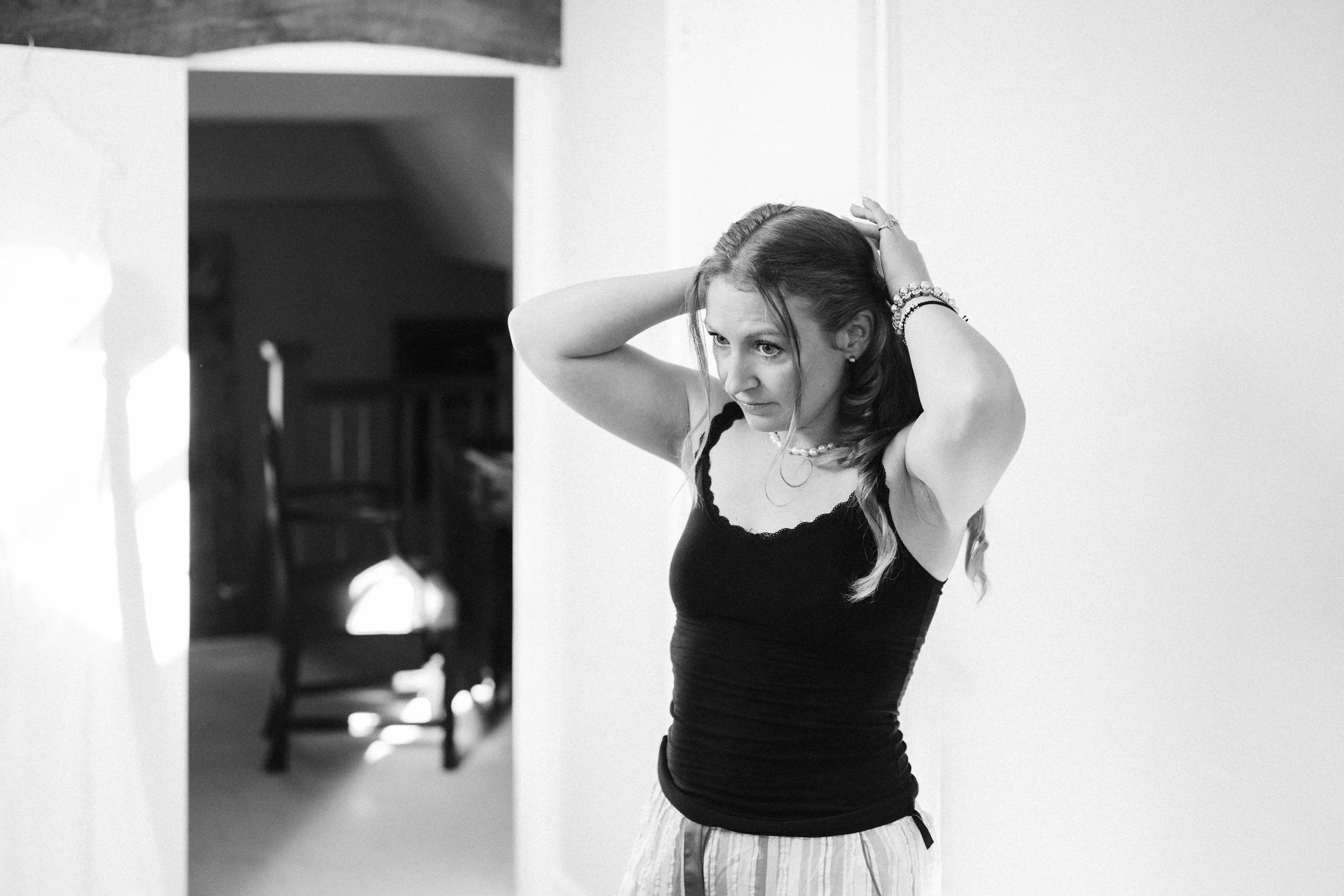 A woman adjusting her hair in front of a plain wall.