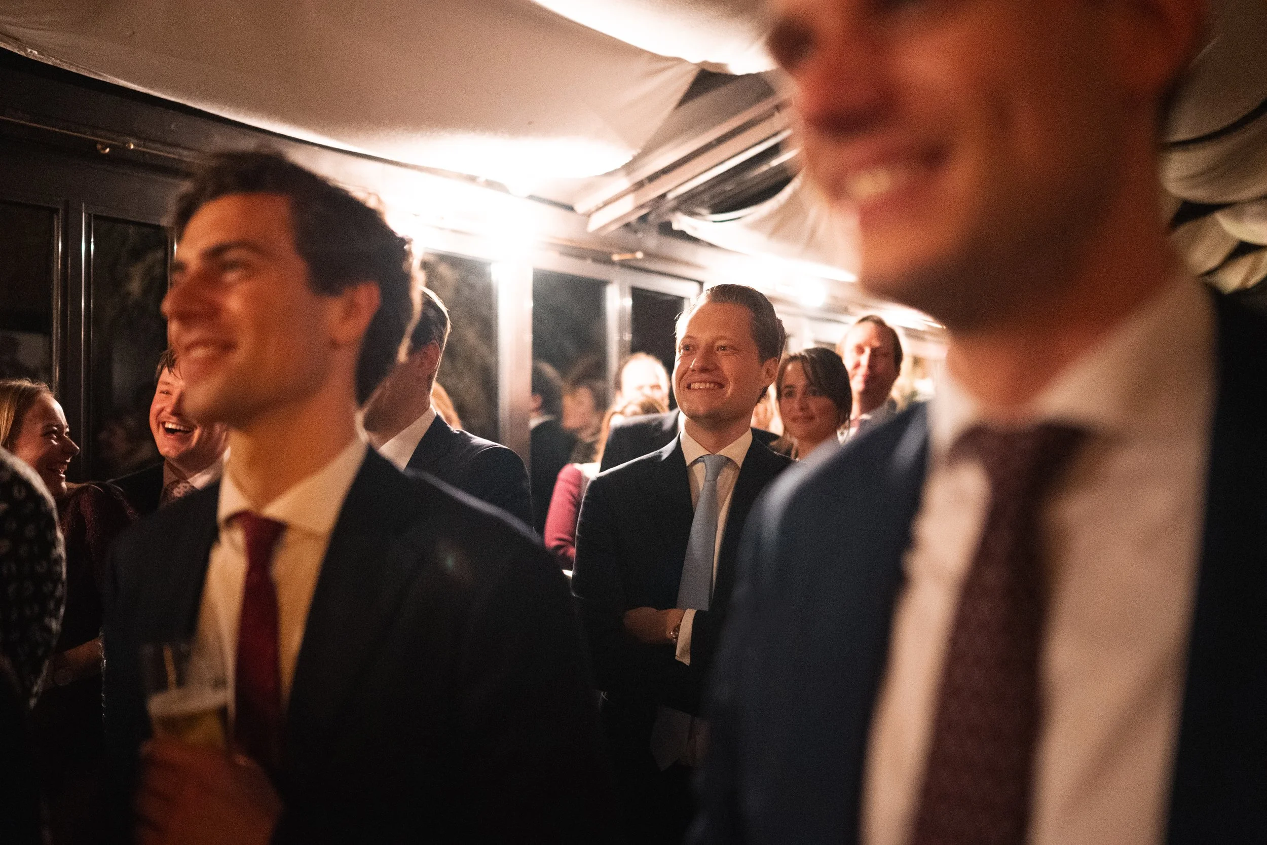Group of people in formal attire at an indoor event, smiling and laughing, with some holding drinks.