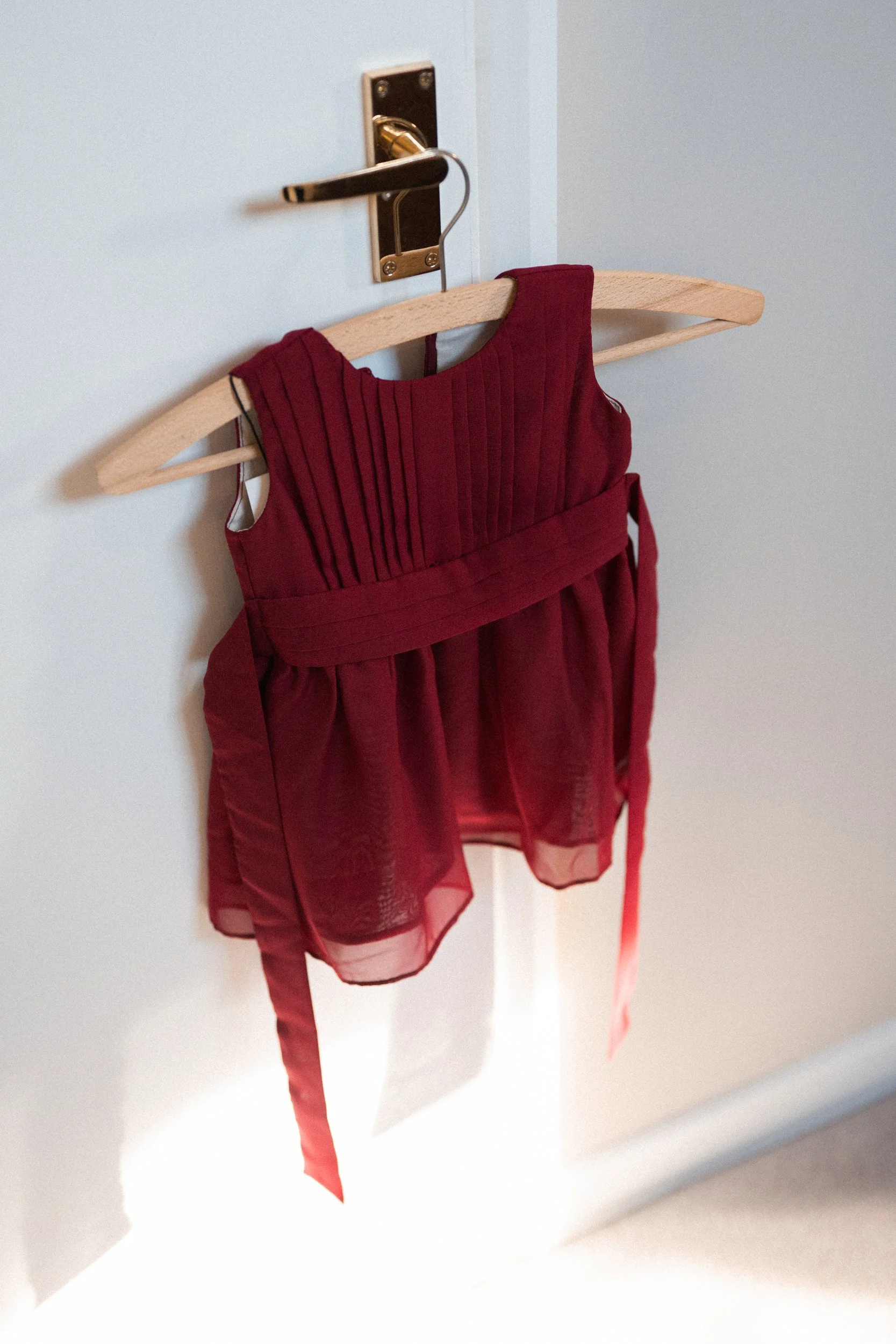 Red sleeveless dress with pleated bodice hanging on a wooden hanger on a white door.