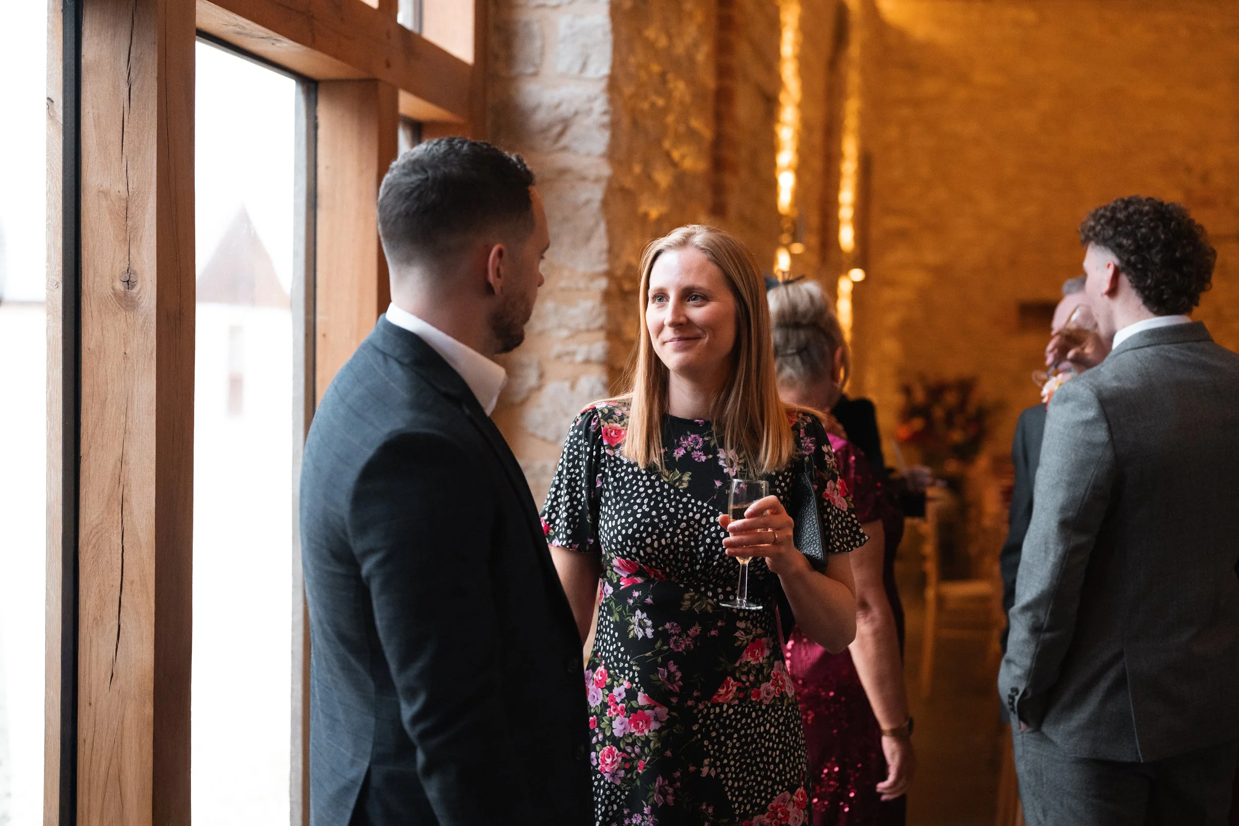 People socializing at a reception inside a venue with wooden and brick walls, some holding drinks.