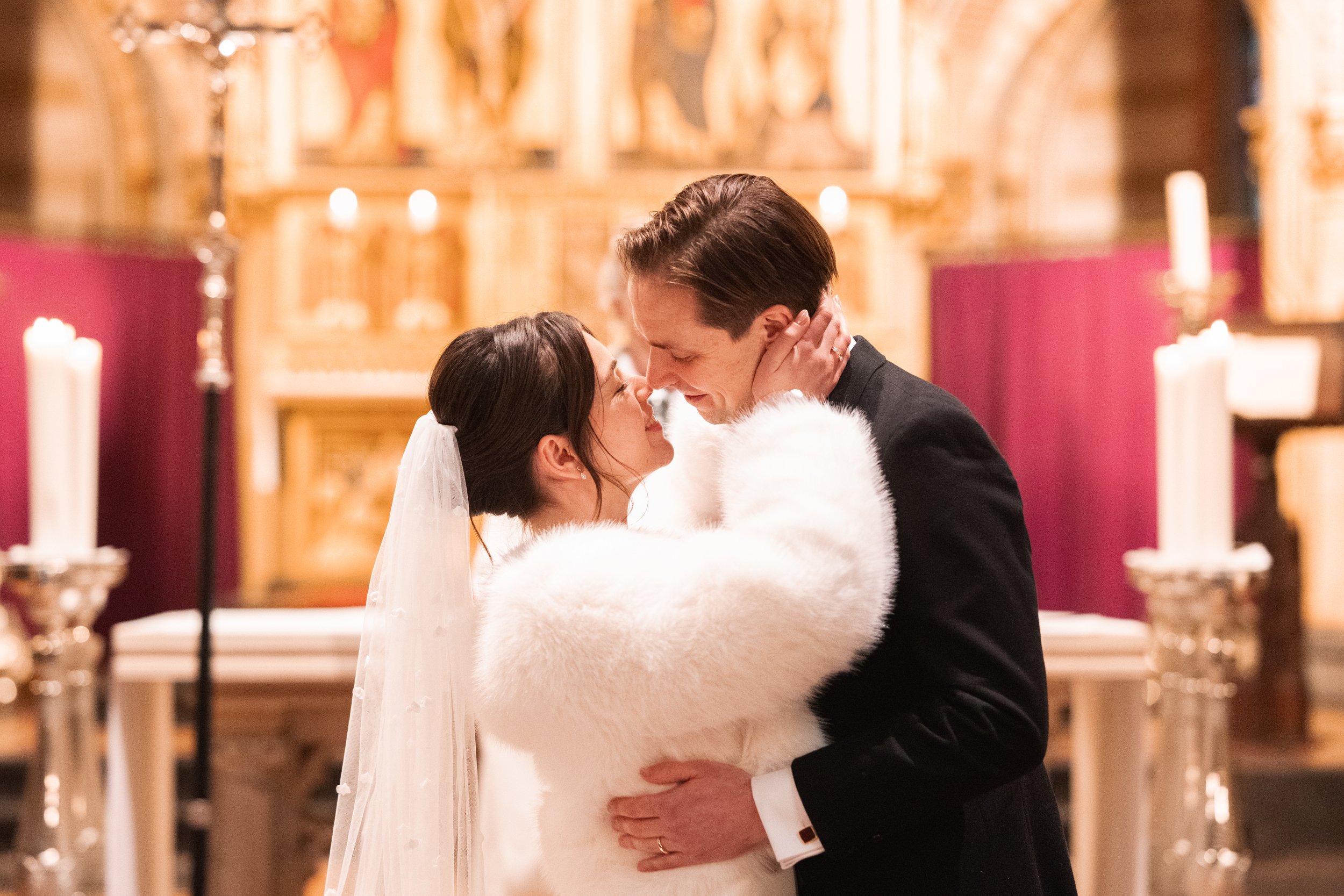A bride and groom sharing a close, intimate moment inside a church with candles, liturgical decor, and a golden altar.