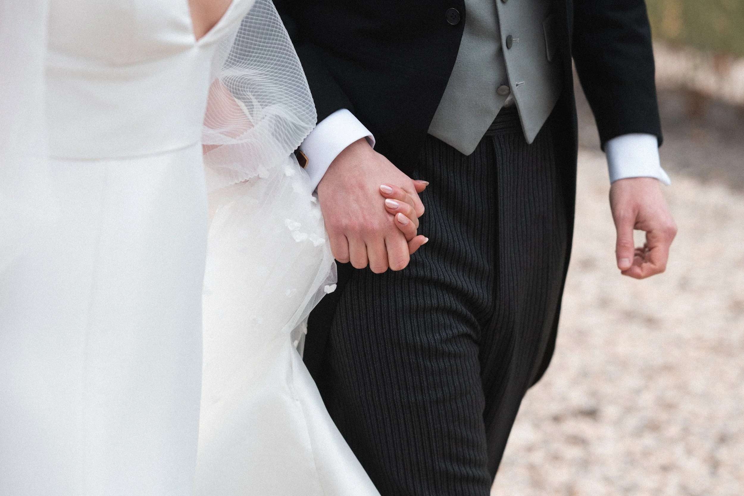 Close-up of a bride and groom holding hands, walking outdoors.