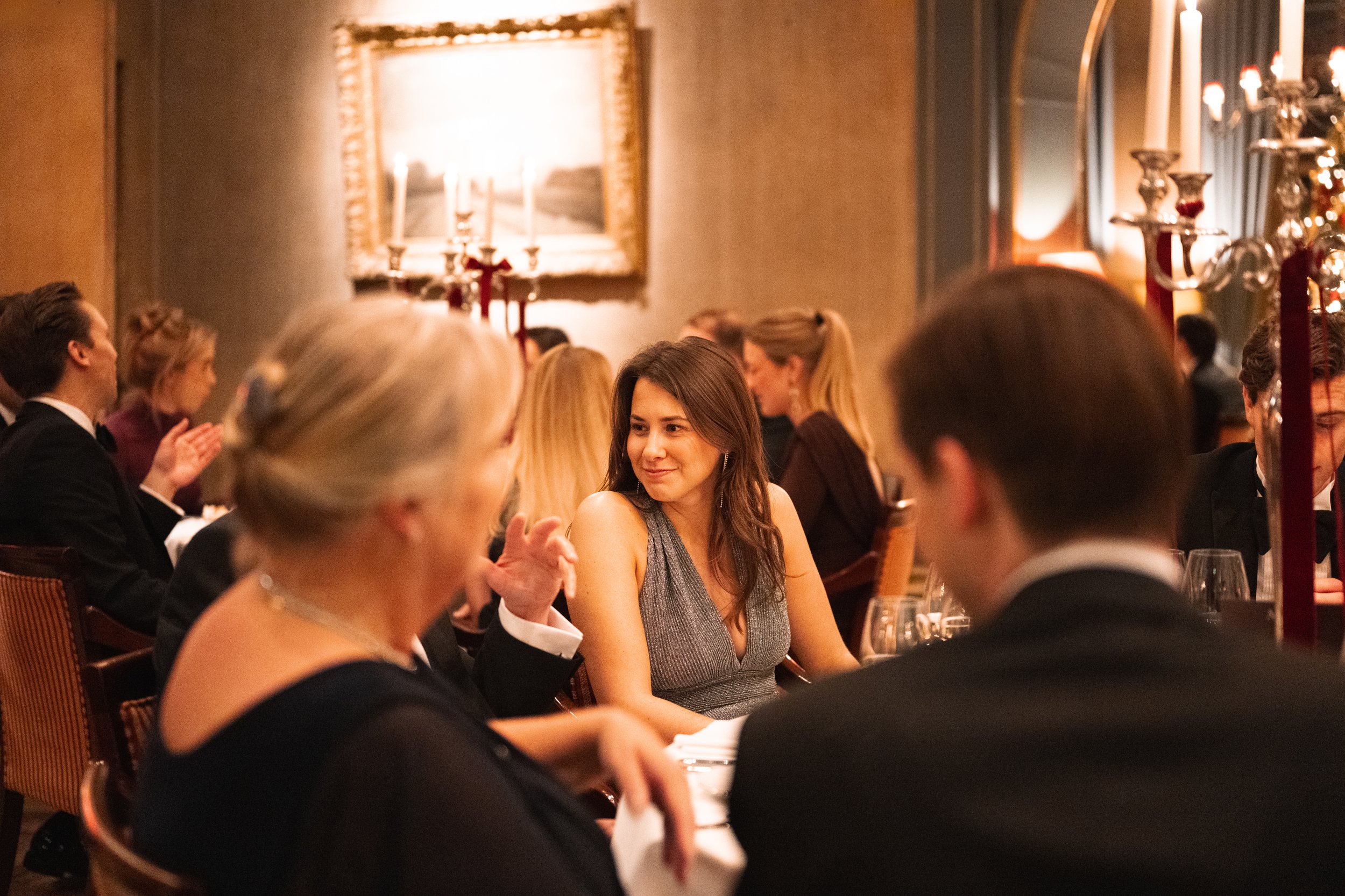 People dressed in formal attire dining at a banquet table in an elegant, candlelit restaurant.