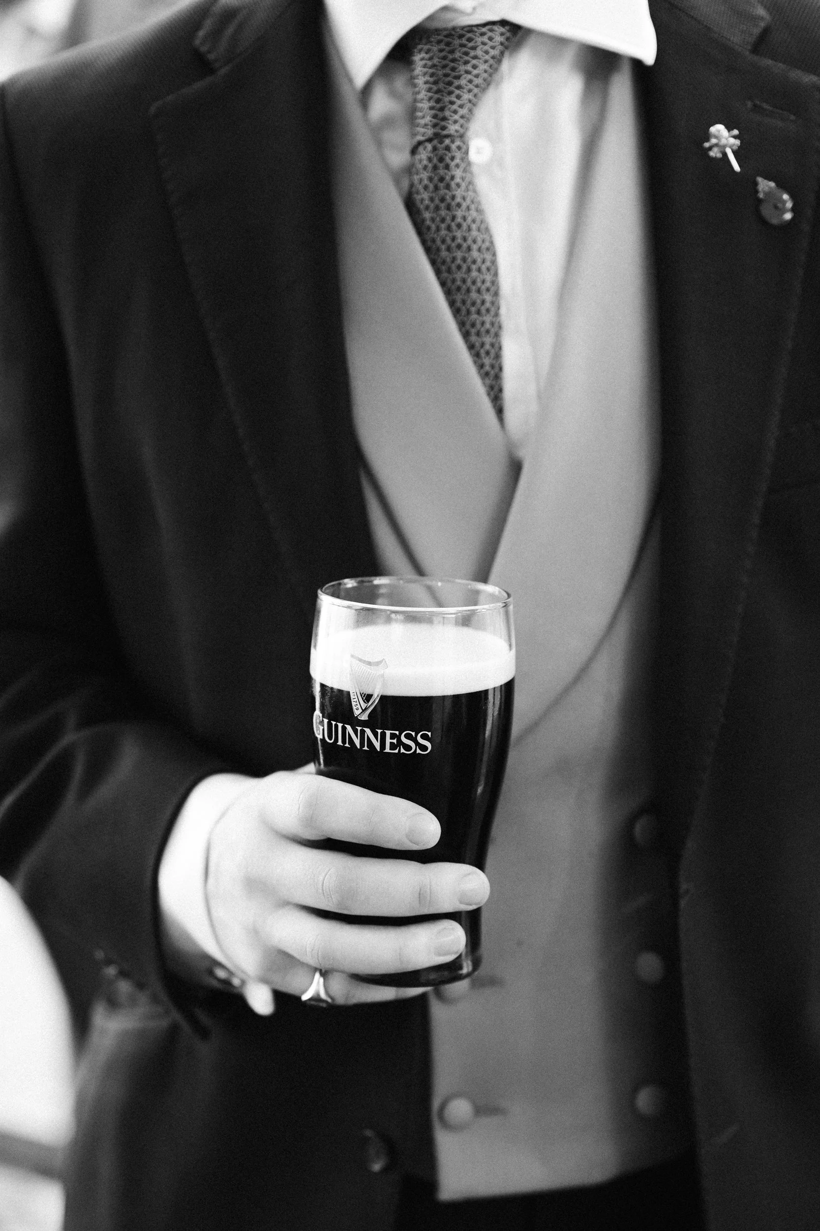 Person in a suit holding a pint of Guinness beer.