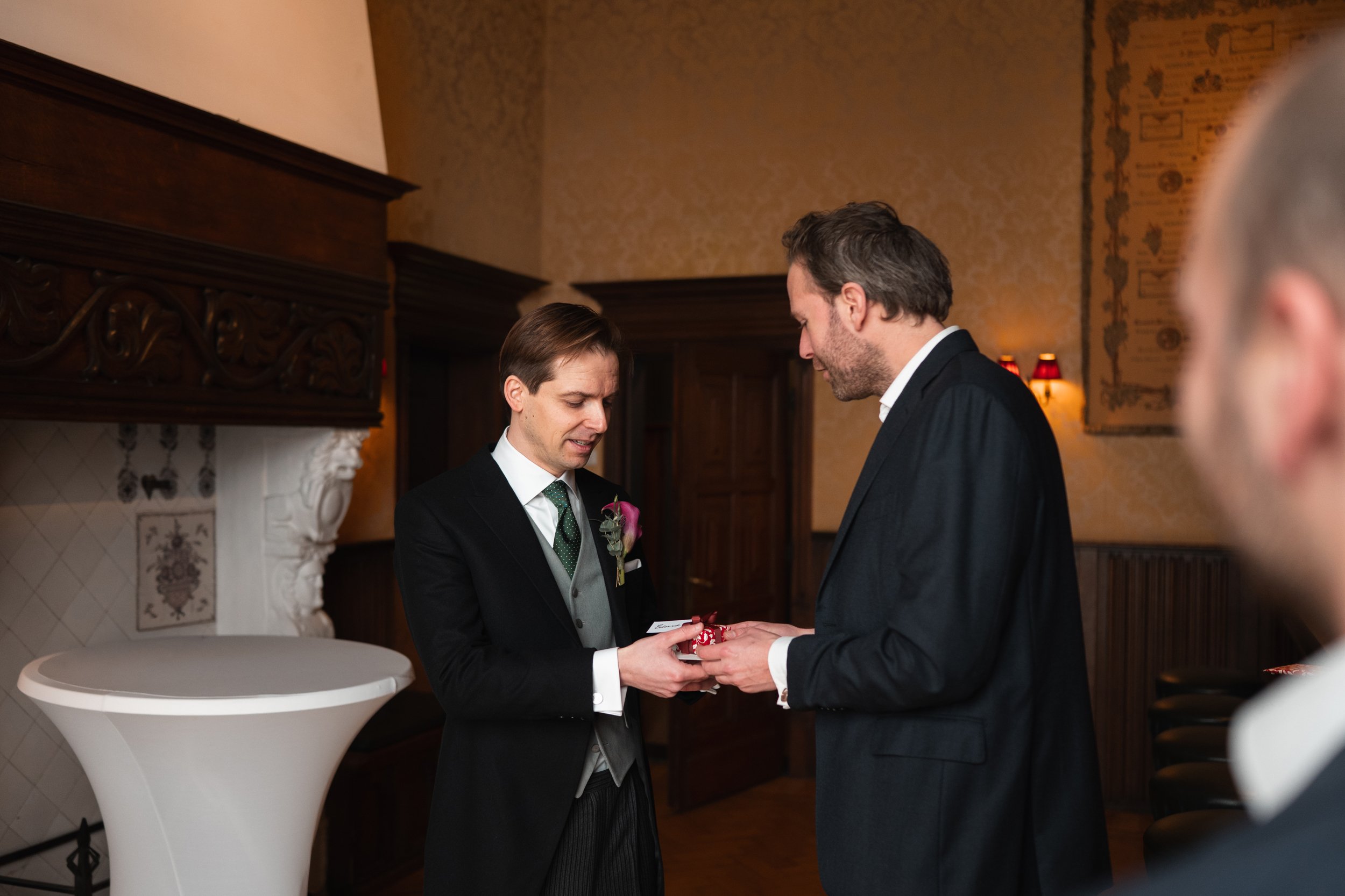Two men in formal suits exchanging rings during a wedding ceremony in an elegant room.