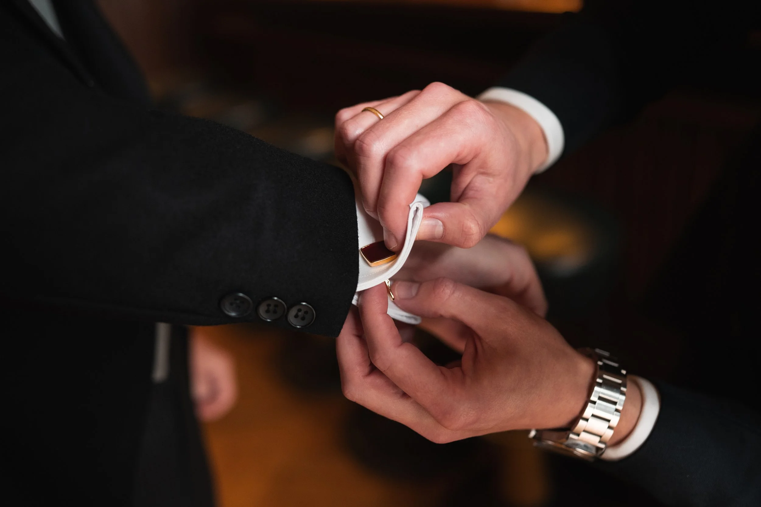 Someone adjusts a tuxedo cufflink on a man's sleeve during a formal event.