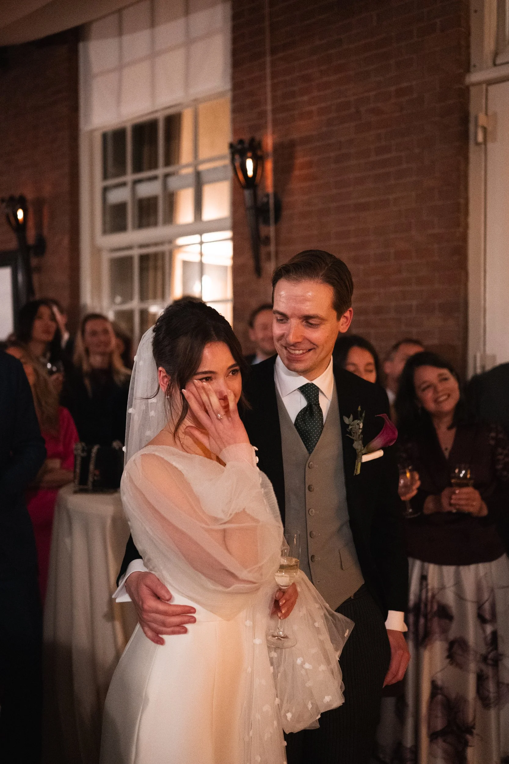 A bride and groom sharing an emotional moment, surrounded by wedding guests at a reception.