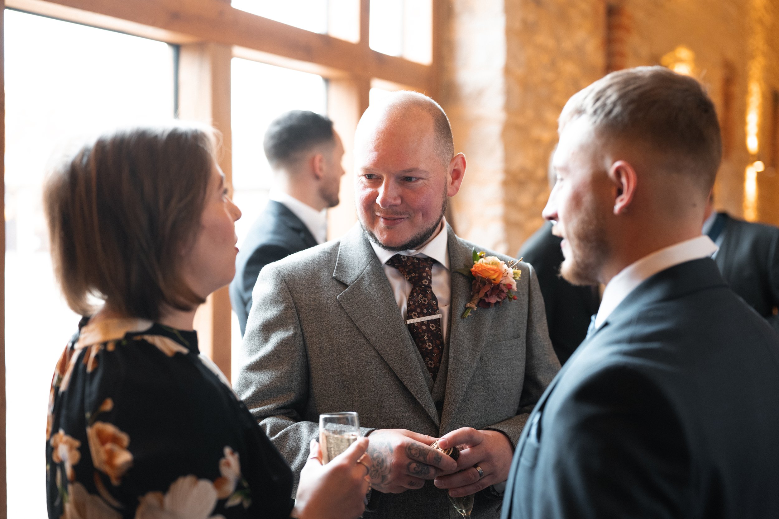 Three people in formal attire engaged in conversation at a social event, with warm lighting and rustic interior.