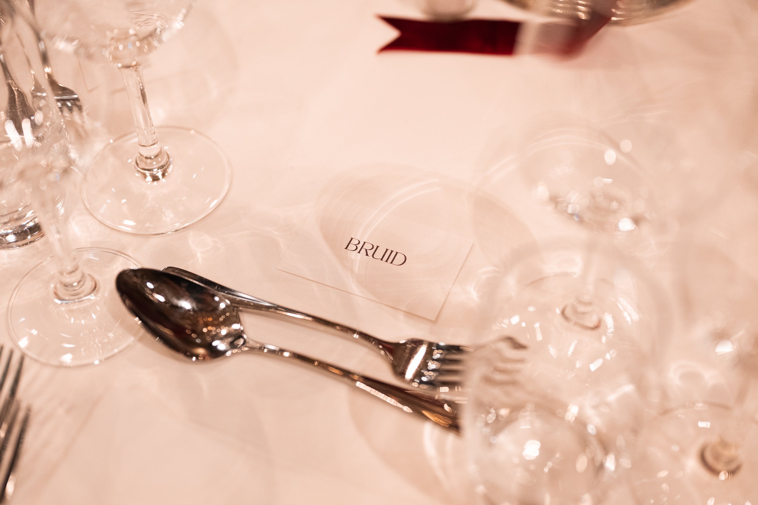 Table setting with a card labeled 'BRIDE', silverware, and multiple empty wine glasses on a white tablecloth.