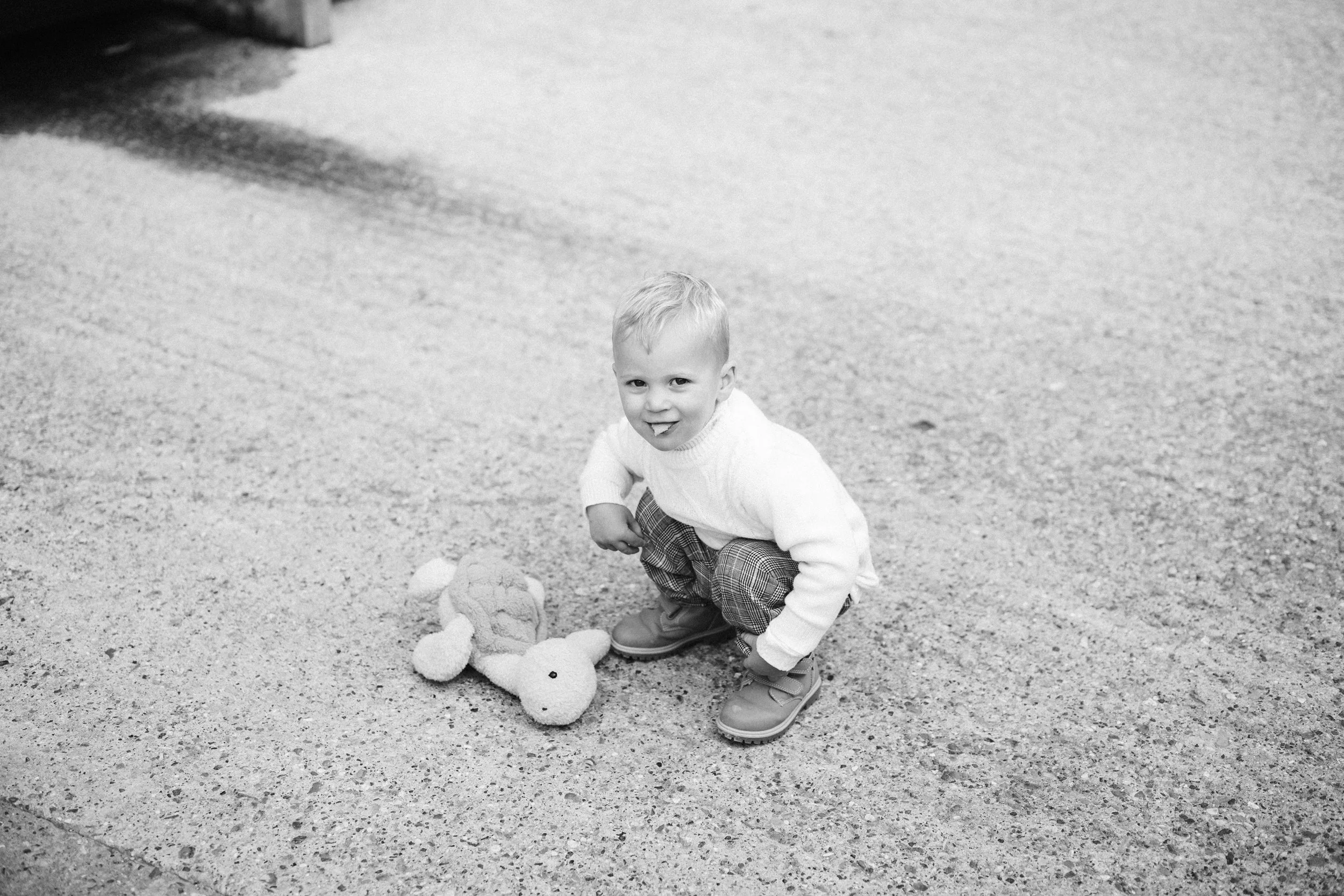 A young child crouching on a textured concrete surface with a stuffed animal toy.