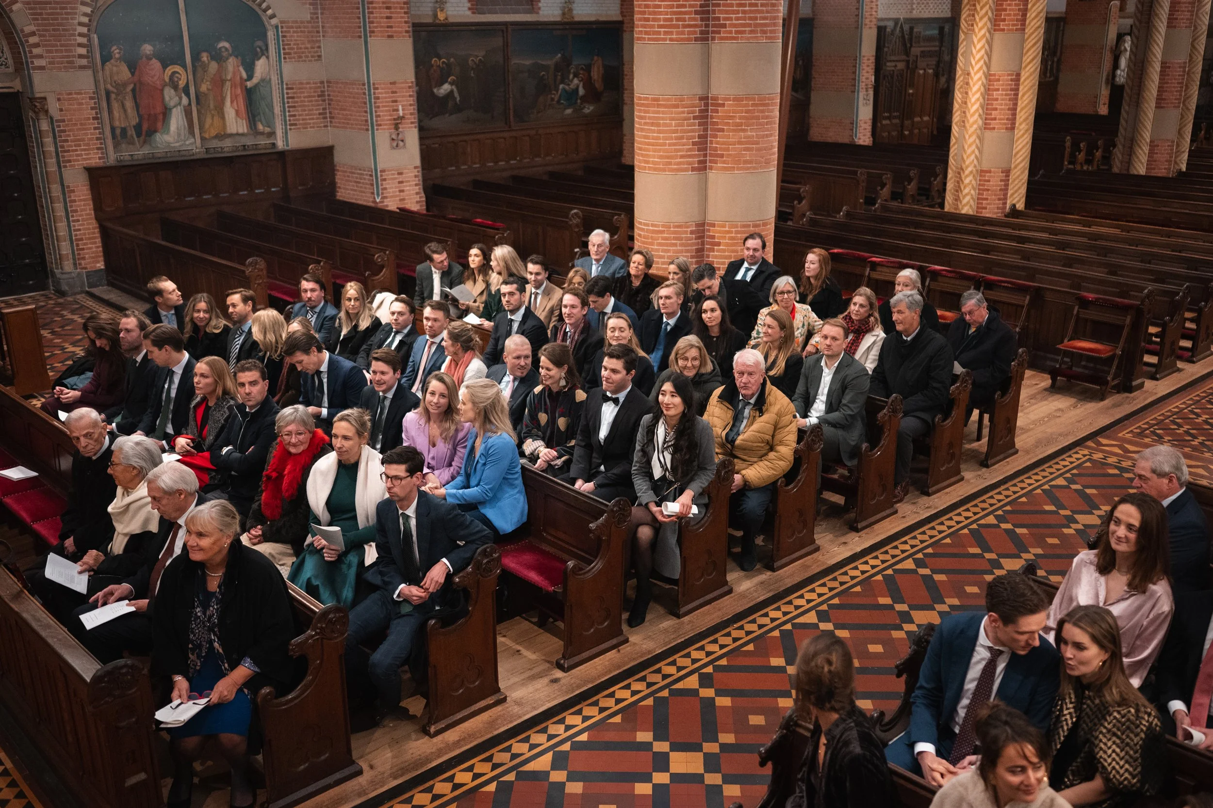 People seated in pews inside a church, attending a service or event, with brick walls and religious artwork in the background.