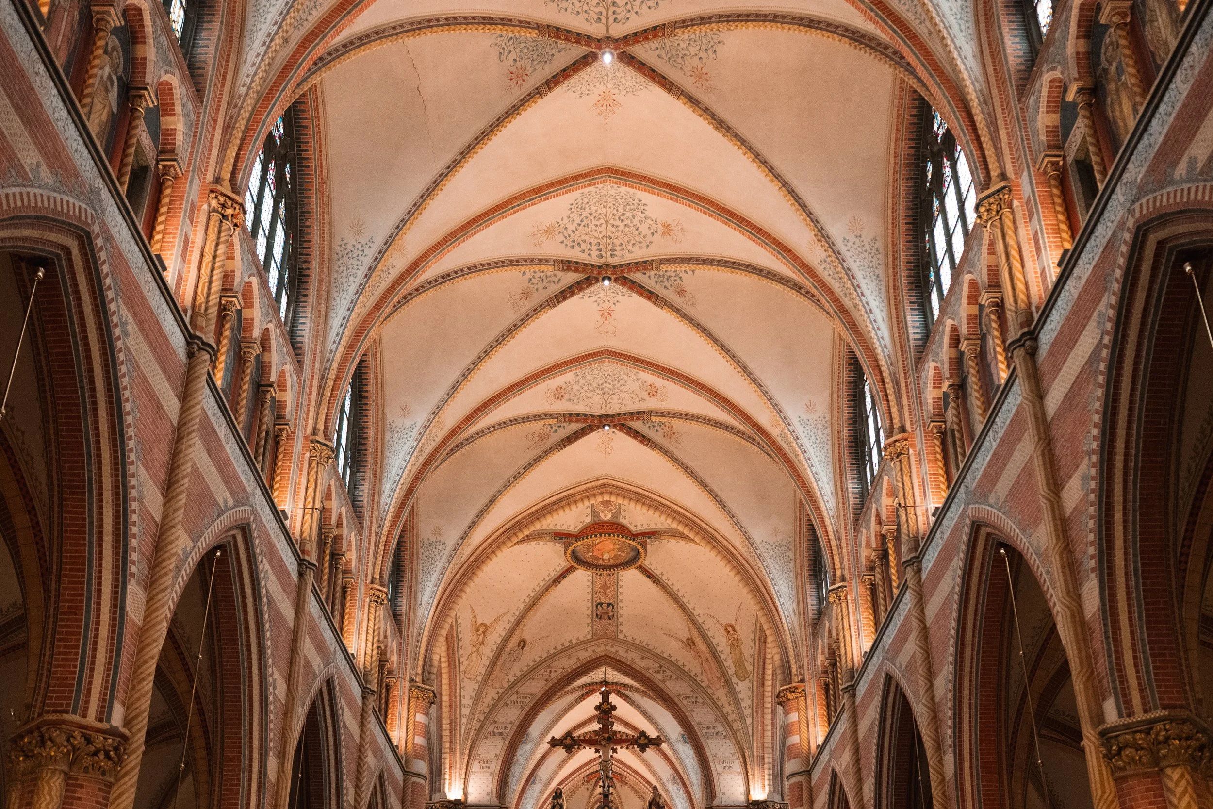 Interior view of a historic church with high vaulted ceilings, decorative arches, and stained glass windows along the sides.