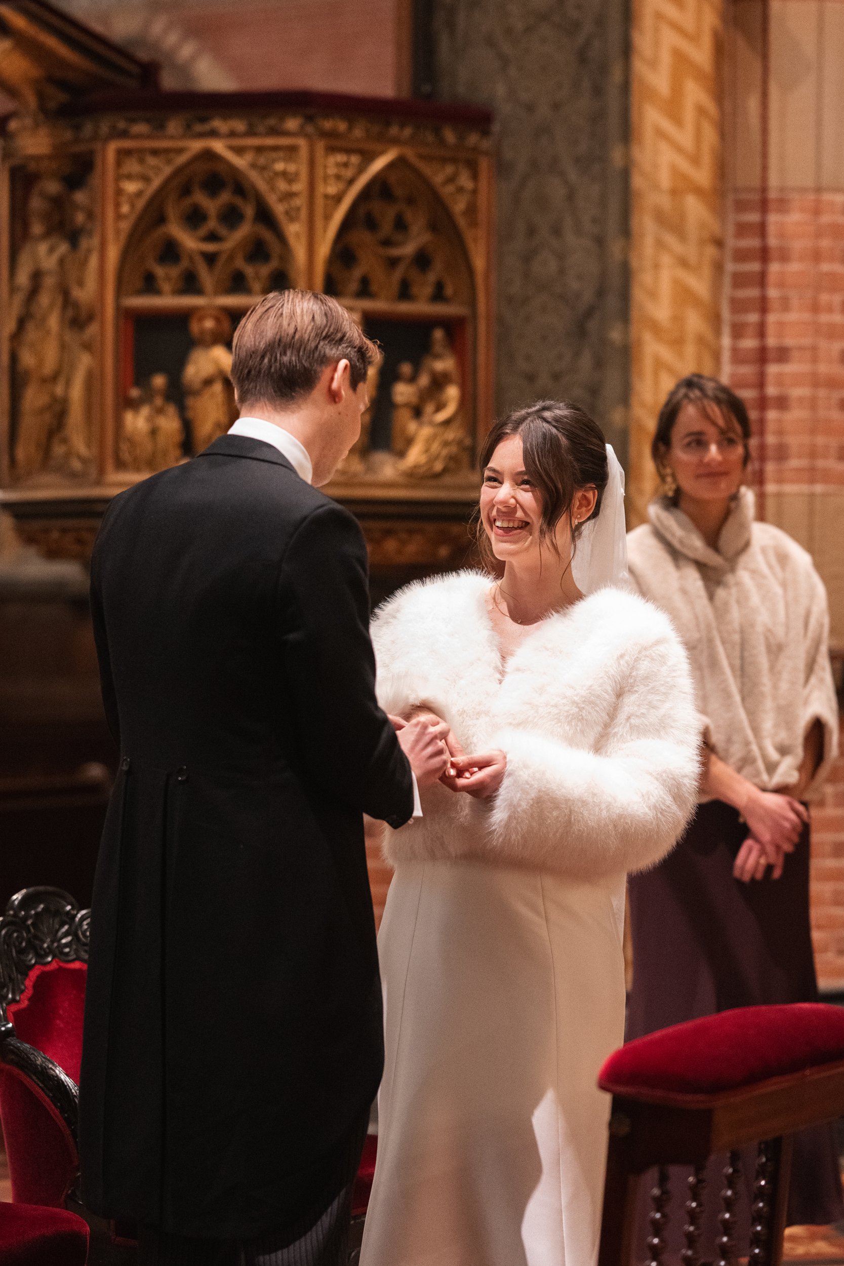 A bride and groom exchanging rings during a wedding ceremony inside a church, with an officiant in the background.