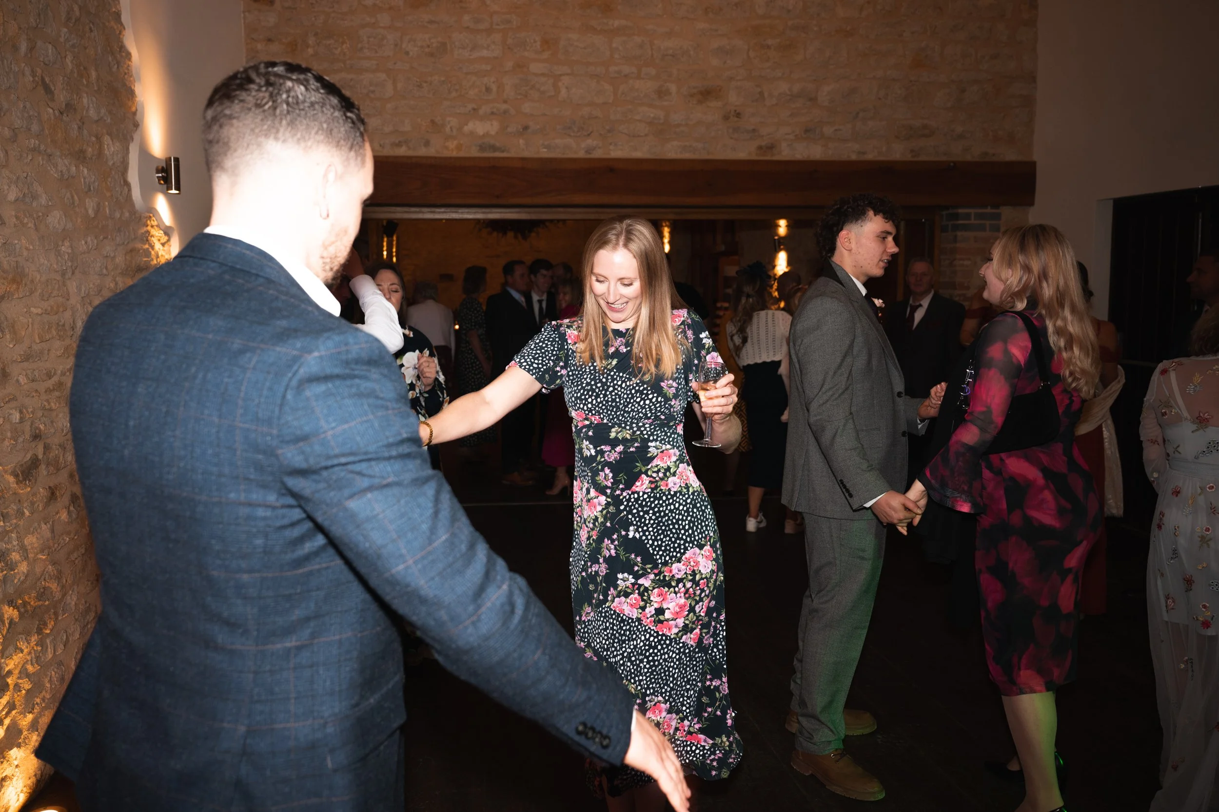 People dancing at a party or wedding reception, enjoying themselves in a warmly lit indoor venue with brick walls.