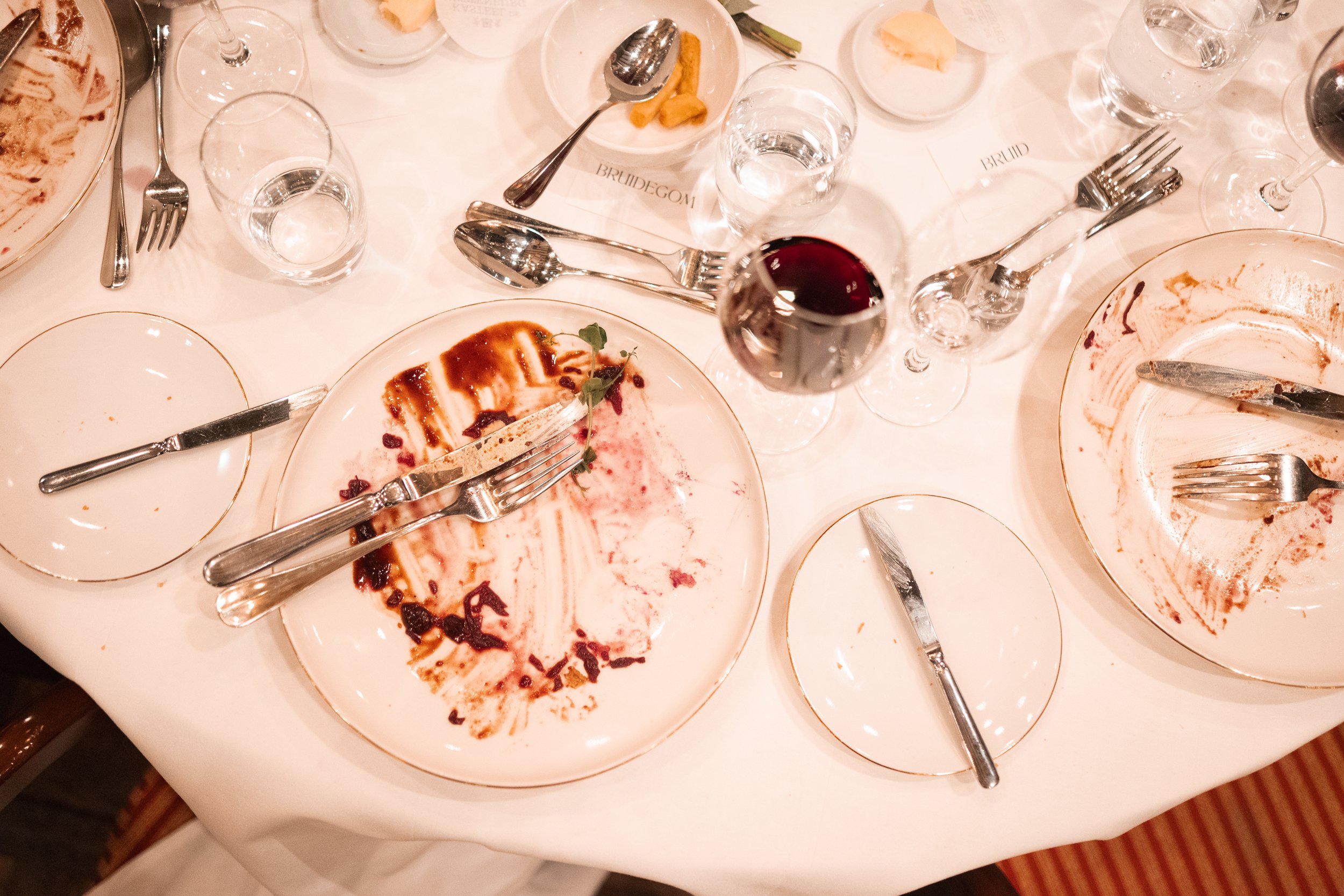Empty dinner plates, glasses, and utensils on a table after a meal, with a glass of red wine in the center.