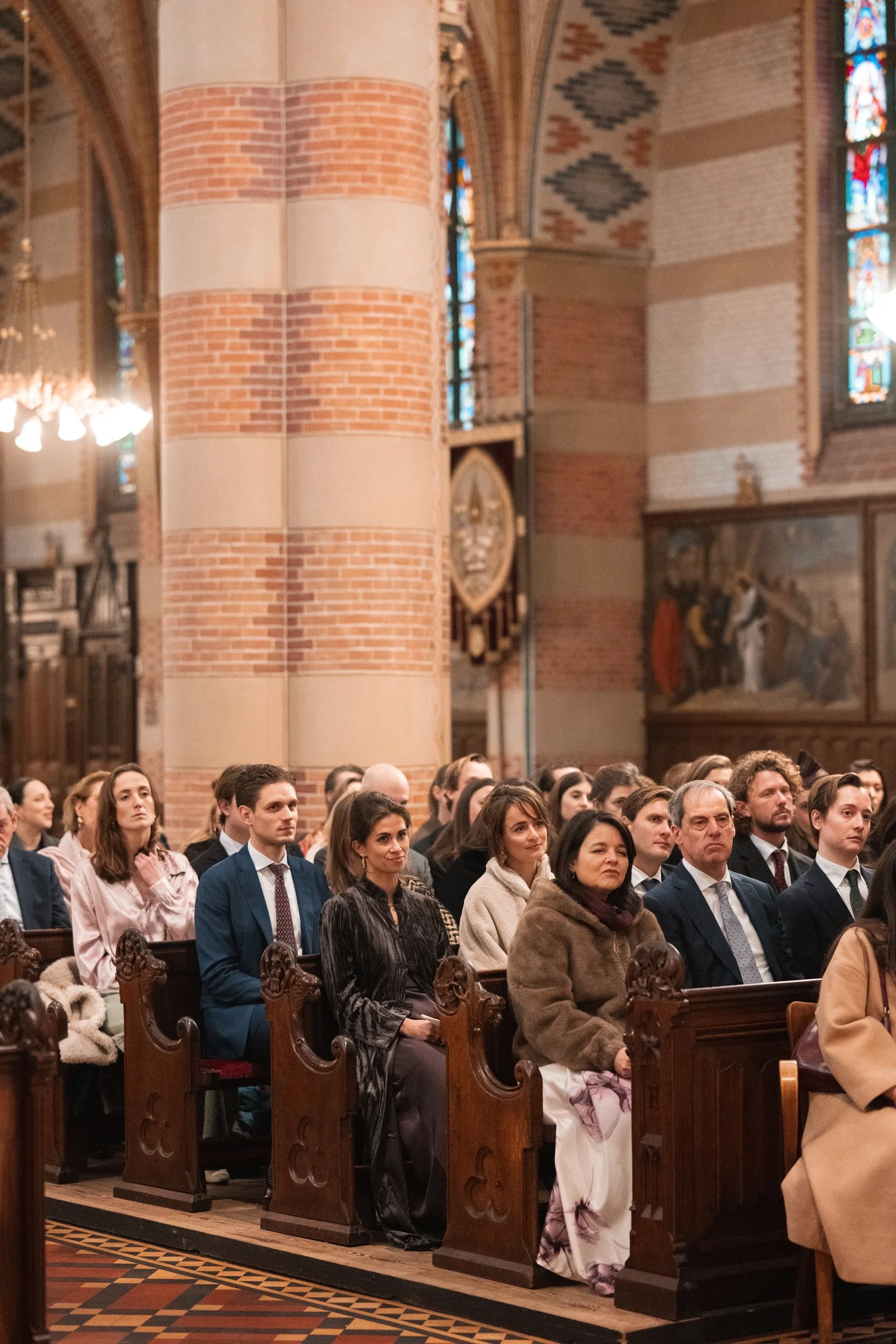 A group of people dressed in formal attire seated inside a church, facing forward during a service or event.
