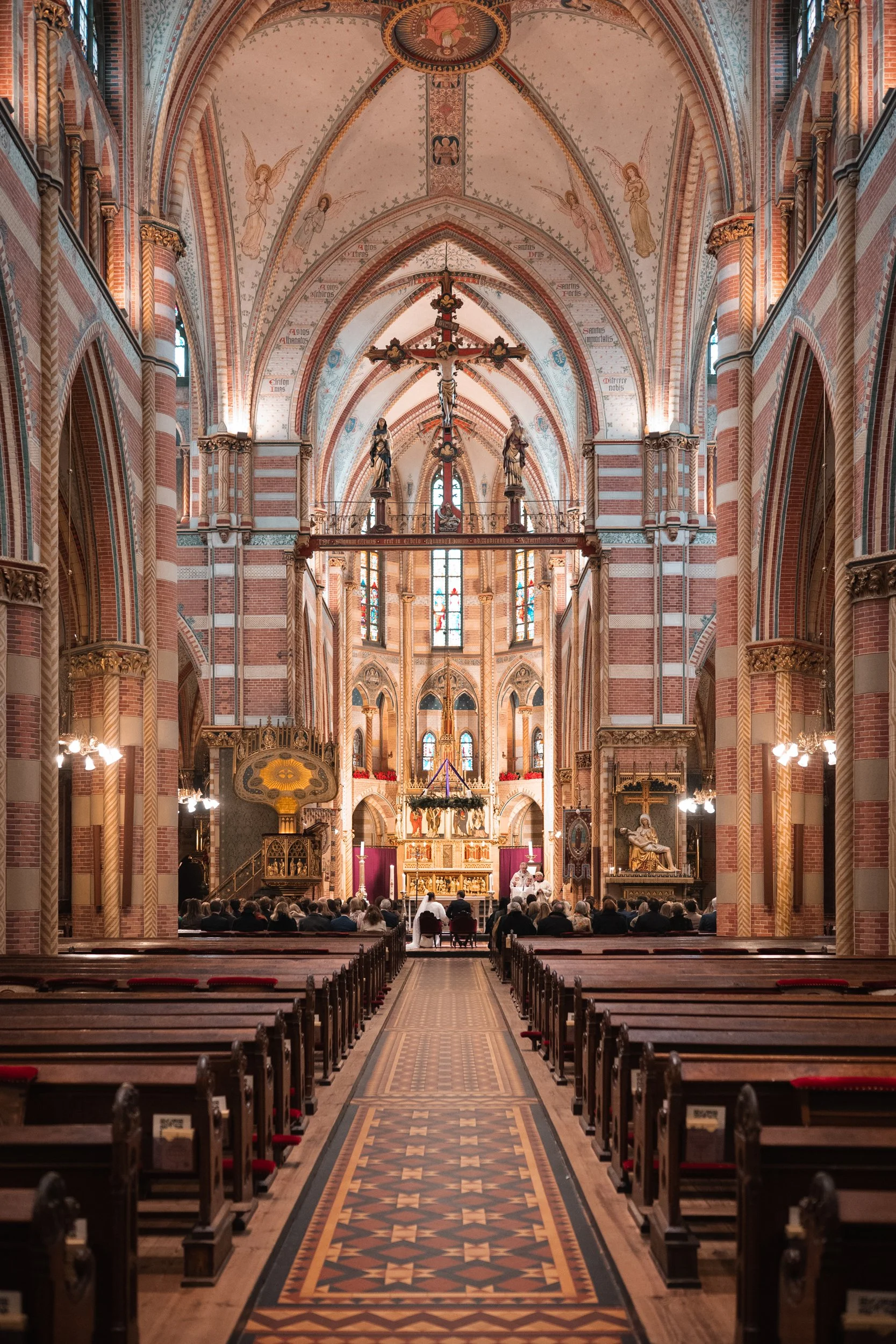 Interior view of a church with high vaulted ceilings, stained glass windows, wooden pews, and an altar at the front, filled with people attending a service.