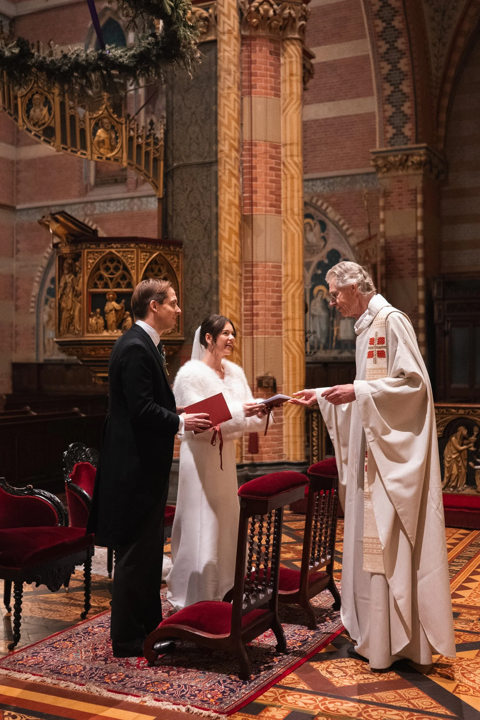 A wedding ceremony inside a church with a pastor officiating, a bride in a white dress and veil, and a groom in a black suit exchanging vows.