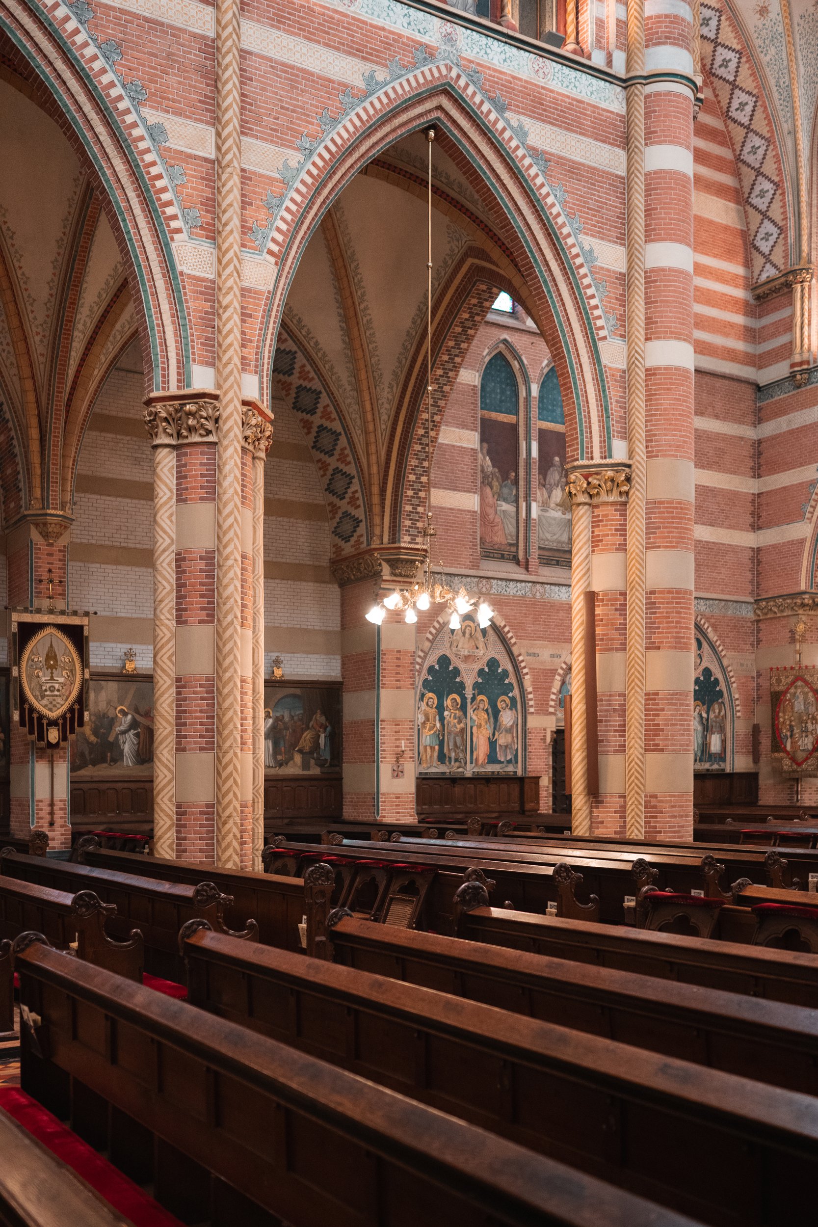 Interior of a church with wooden pews, brick walls, stained glass windows, and ornate decorations including paintings and banners.