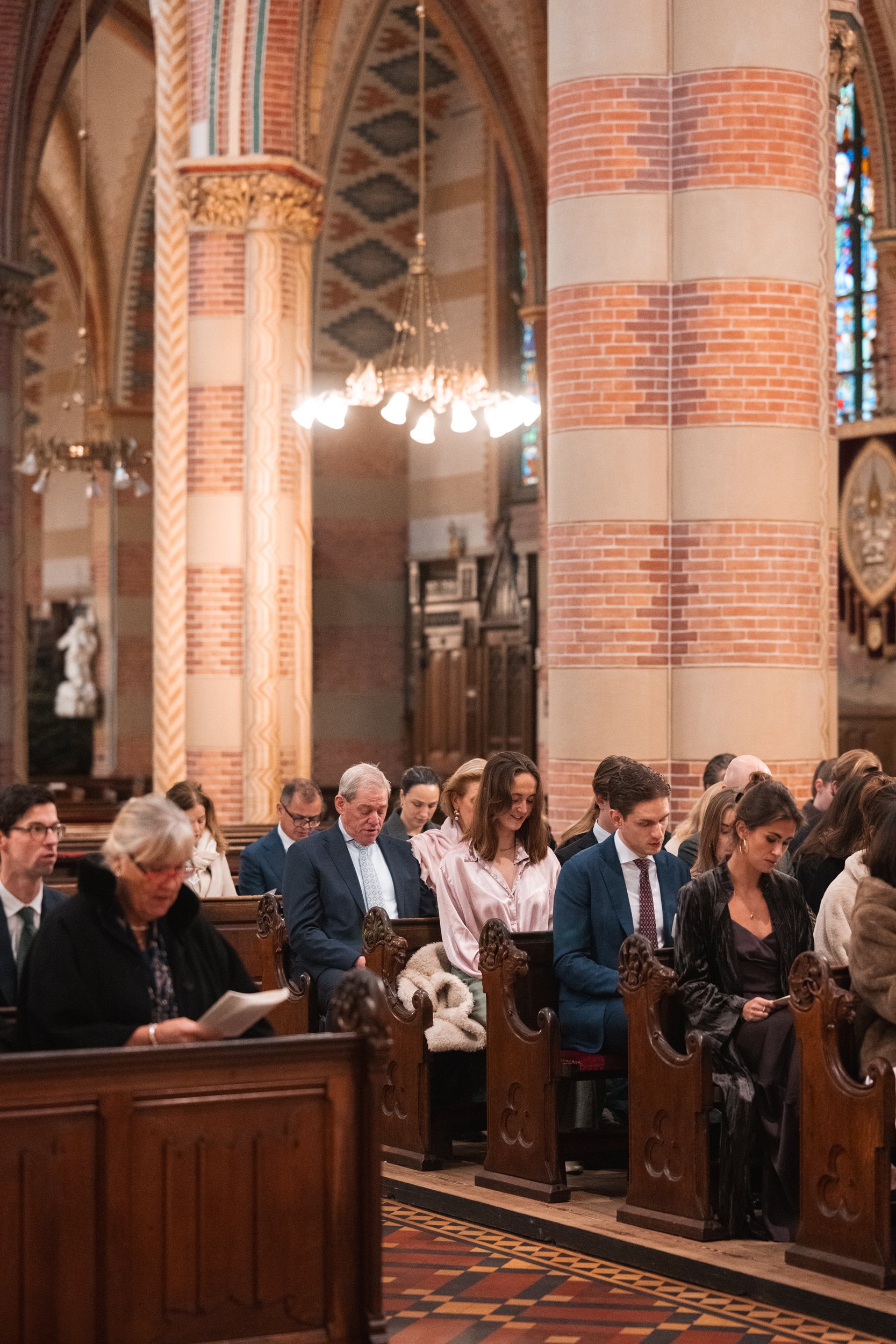 People seated in pews inside a church during a service, with stained glass windows and brick columns in the background.