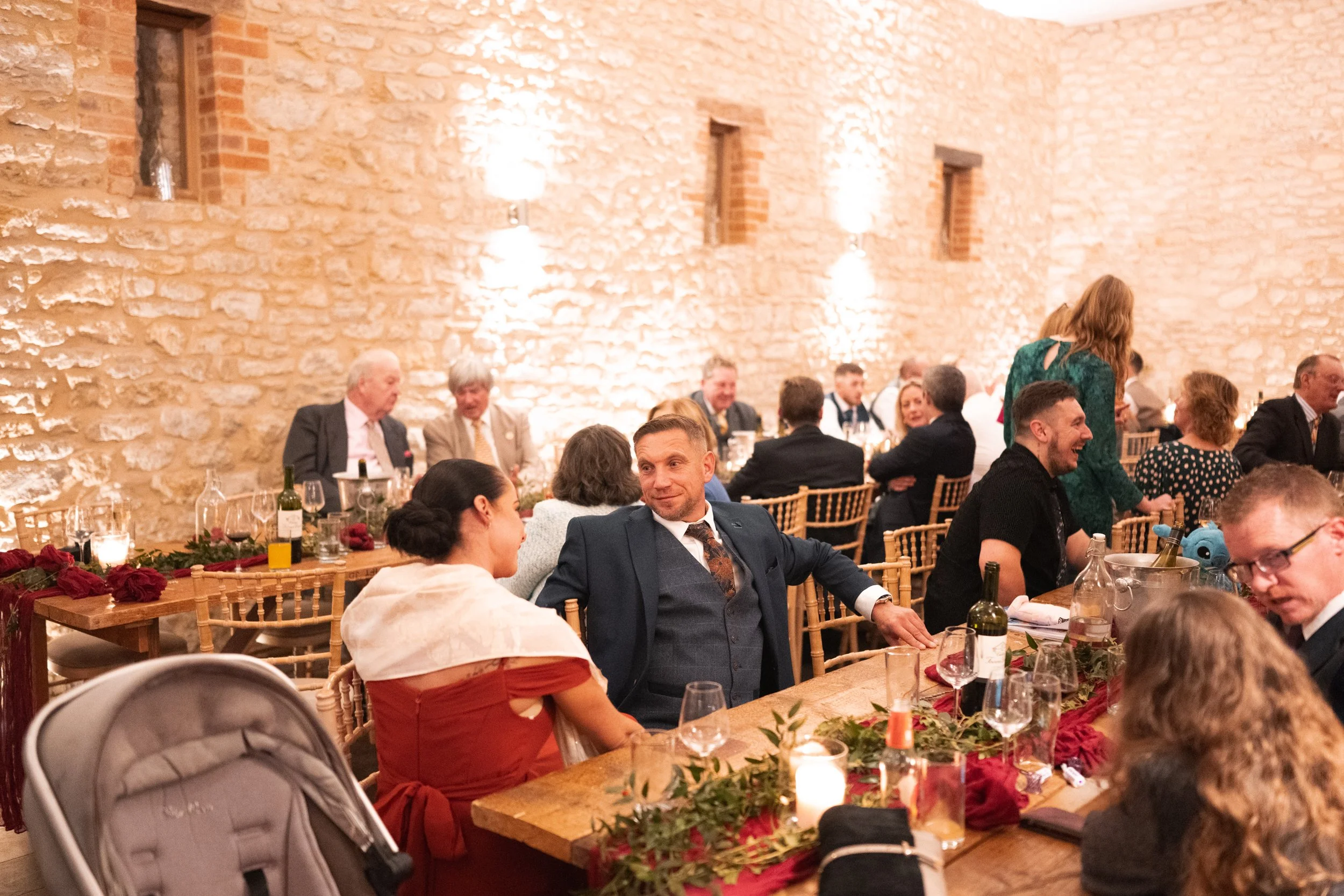 People sitting at a decorated wooden table in a rustic stone-walled banquet hall, enjoying a formal event or wedding reception.