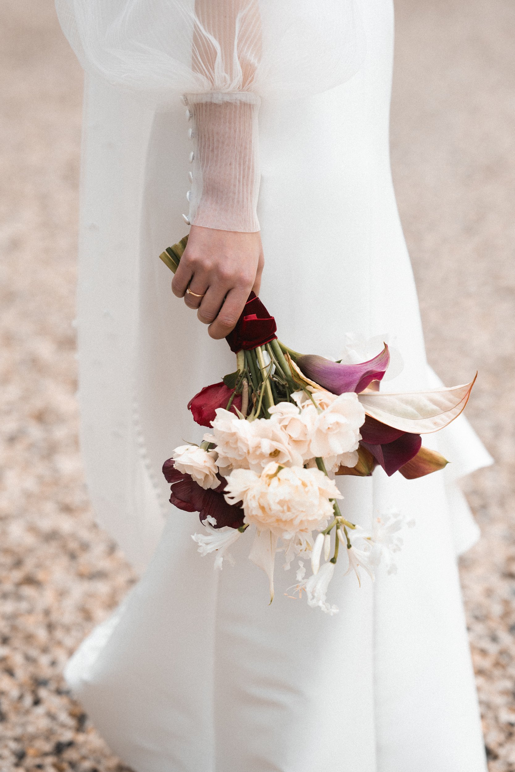 A woman in a white dress holding a bouquet of pink, purple, and white flowers in her right hand, with the focus on her hand and the flowers.