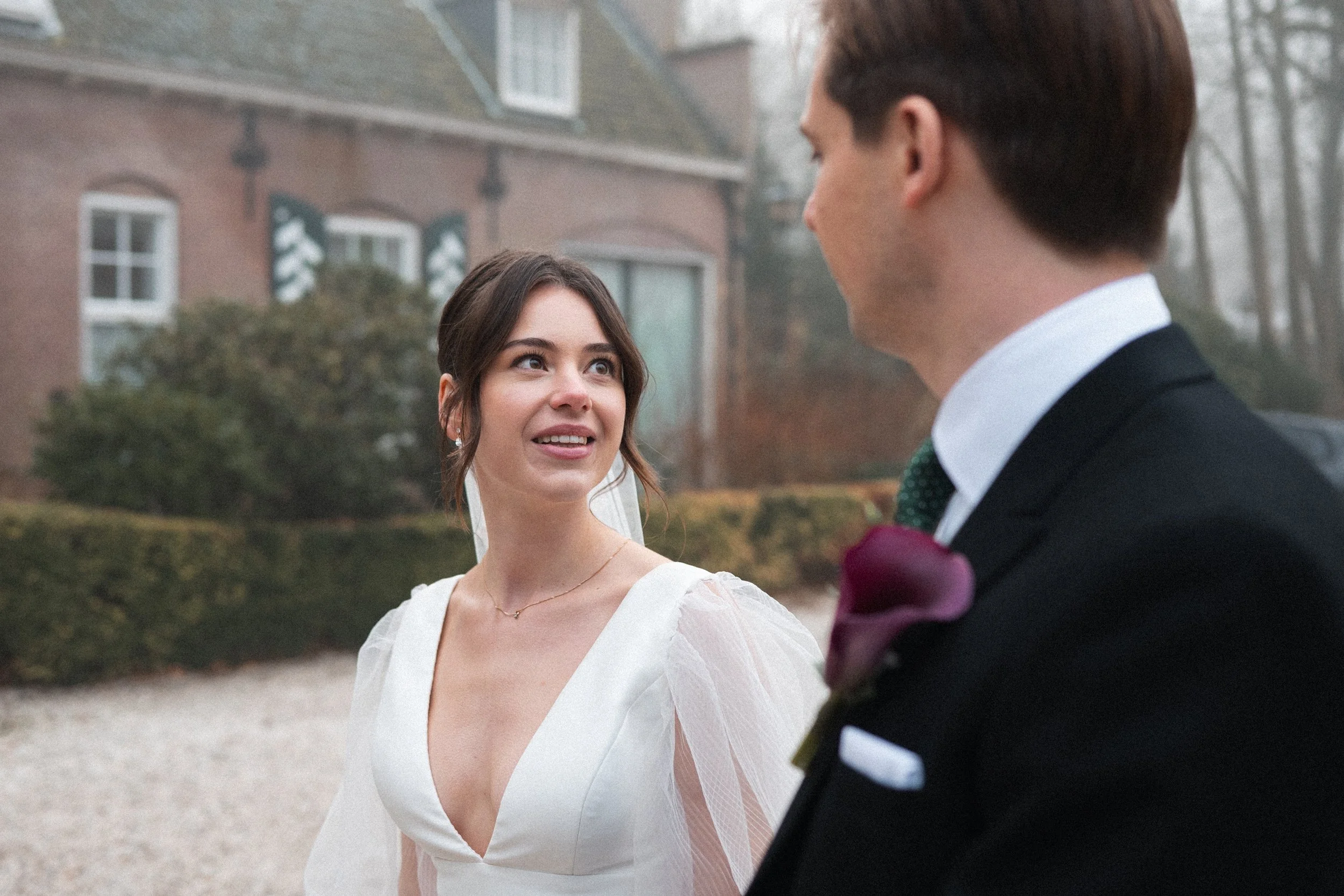 A bride and groom standing outdoors on their wedding day, looking at each other.