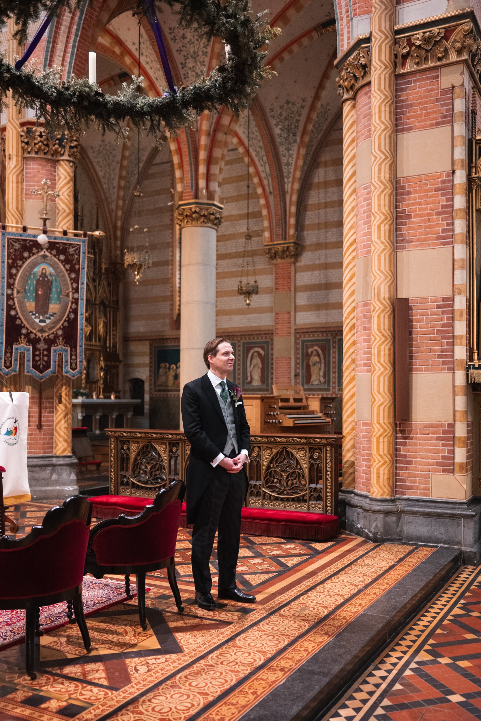 A man dressed in formal attire, standing inside a decorated church with ornate architecture, patterned floor, and religious banners.