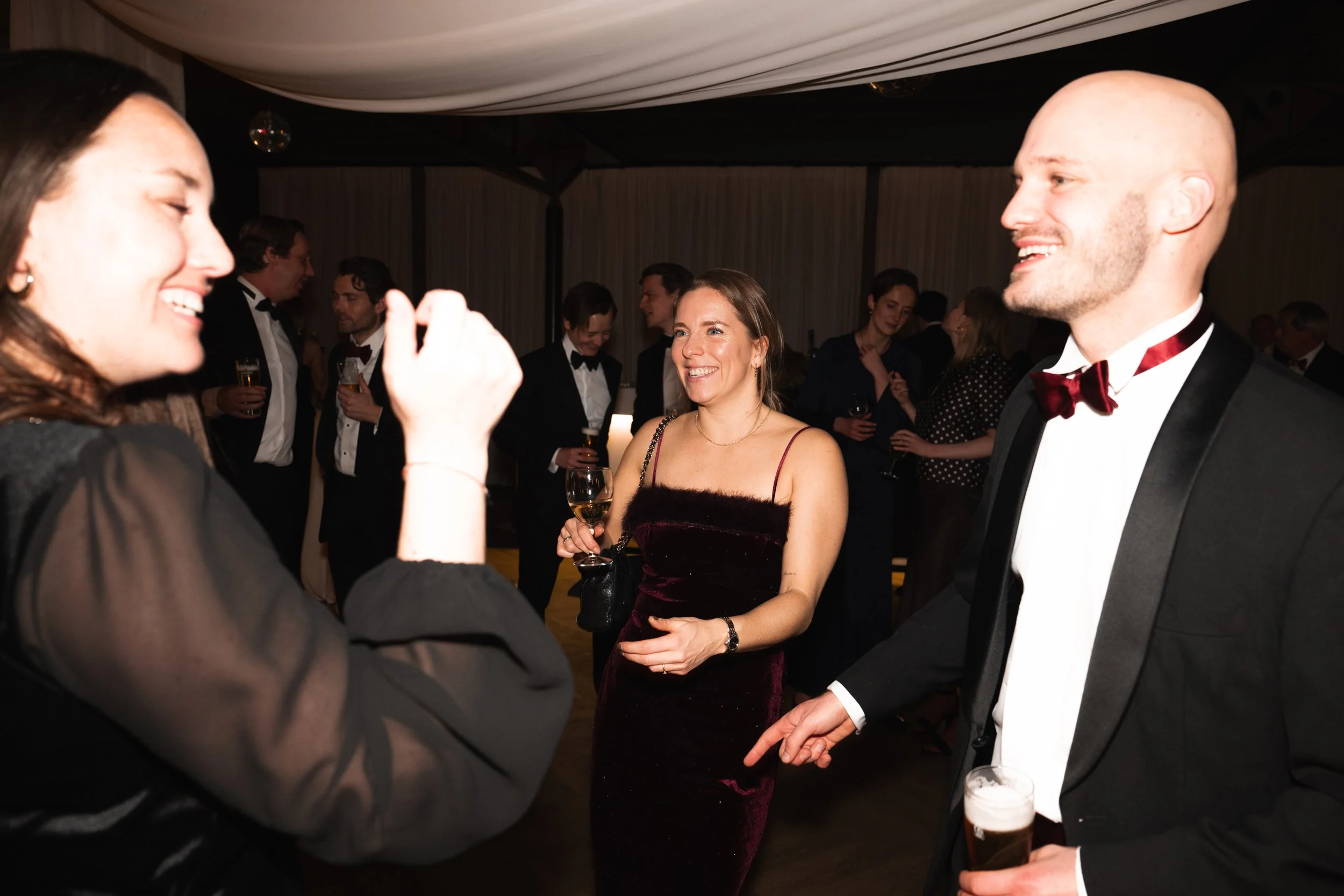 People dressed in formal attire socializing at a party or event, holding drinks and smiling.