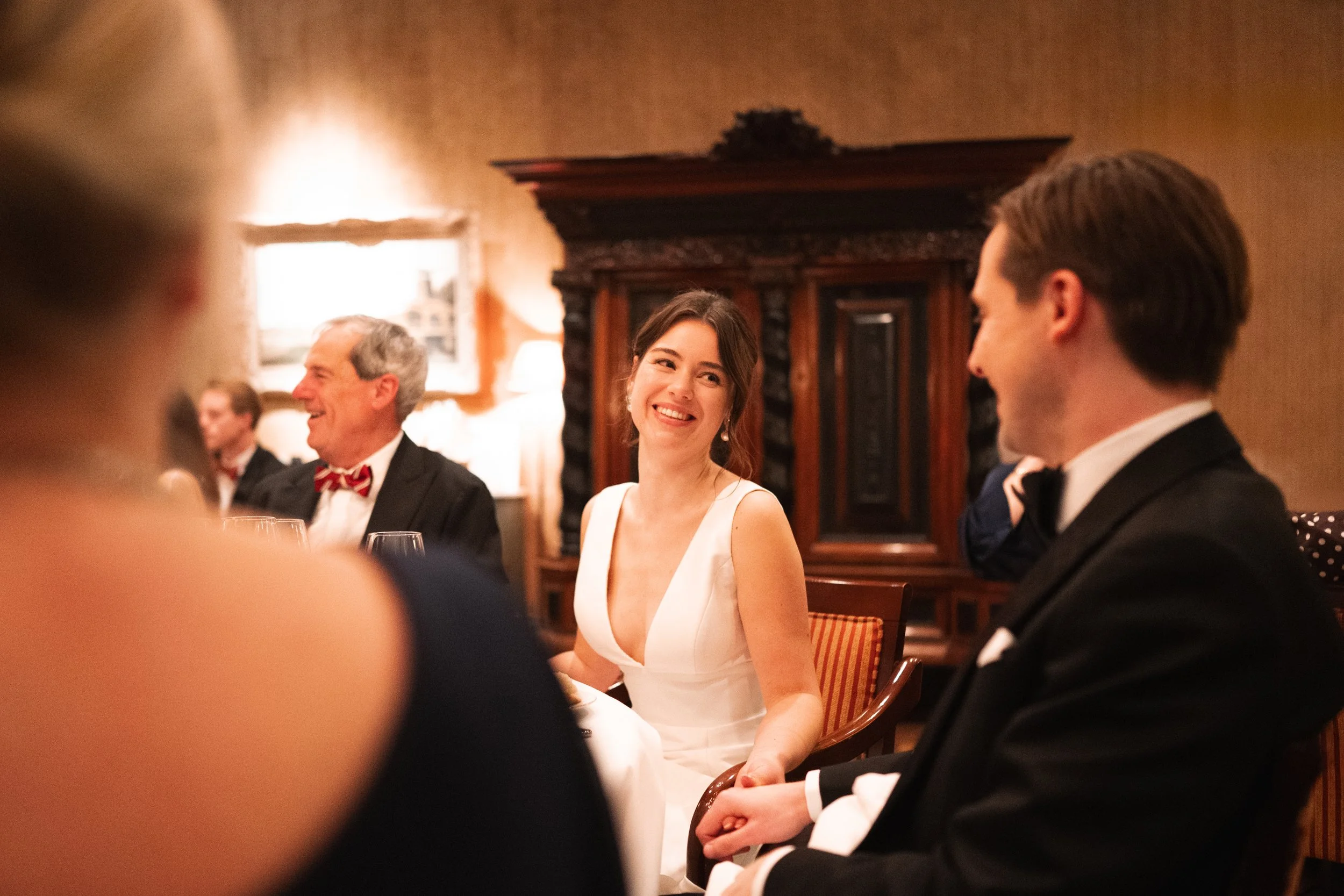 A woman in a white dress smiling at a man in a tuxedo during a formal dinner or celebration.