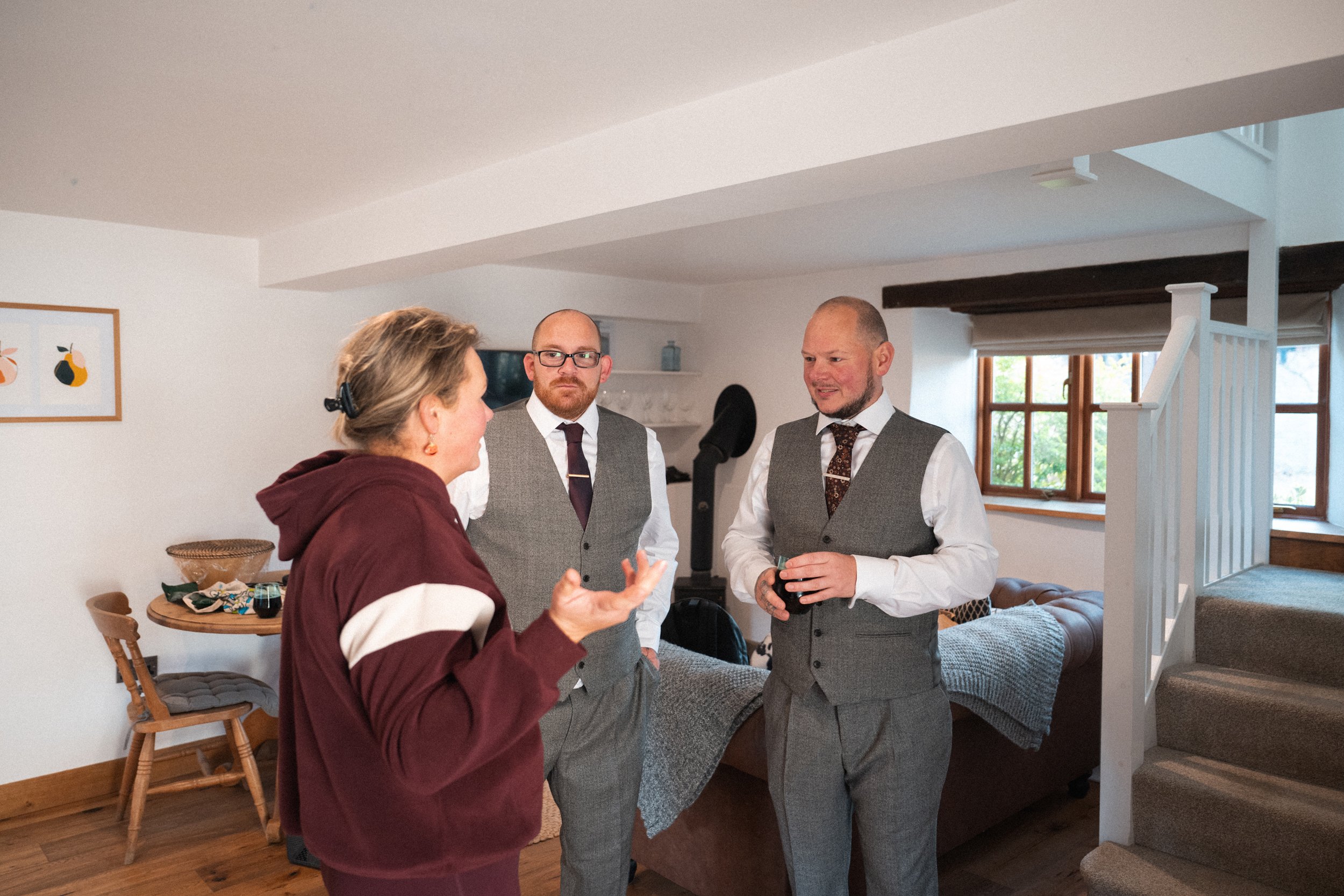 Three men and one woman engaging in conversation inside a cozy living room with large windows and a staircase.