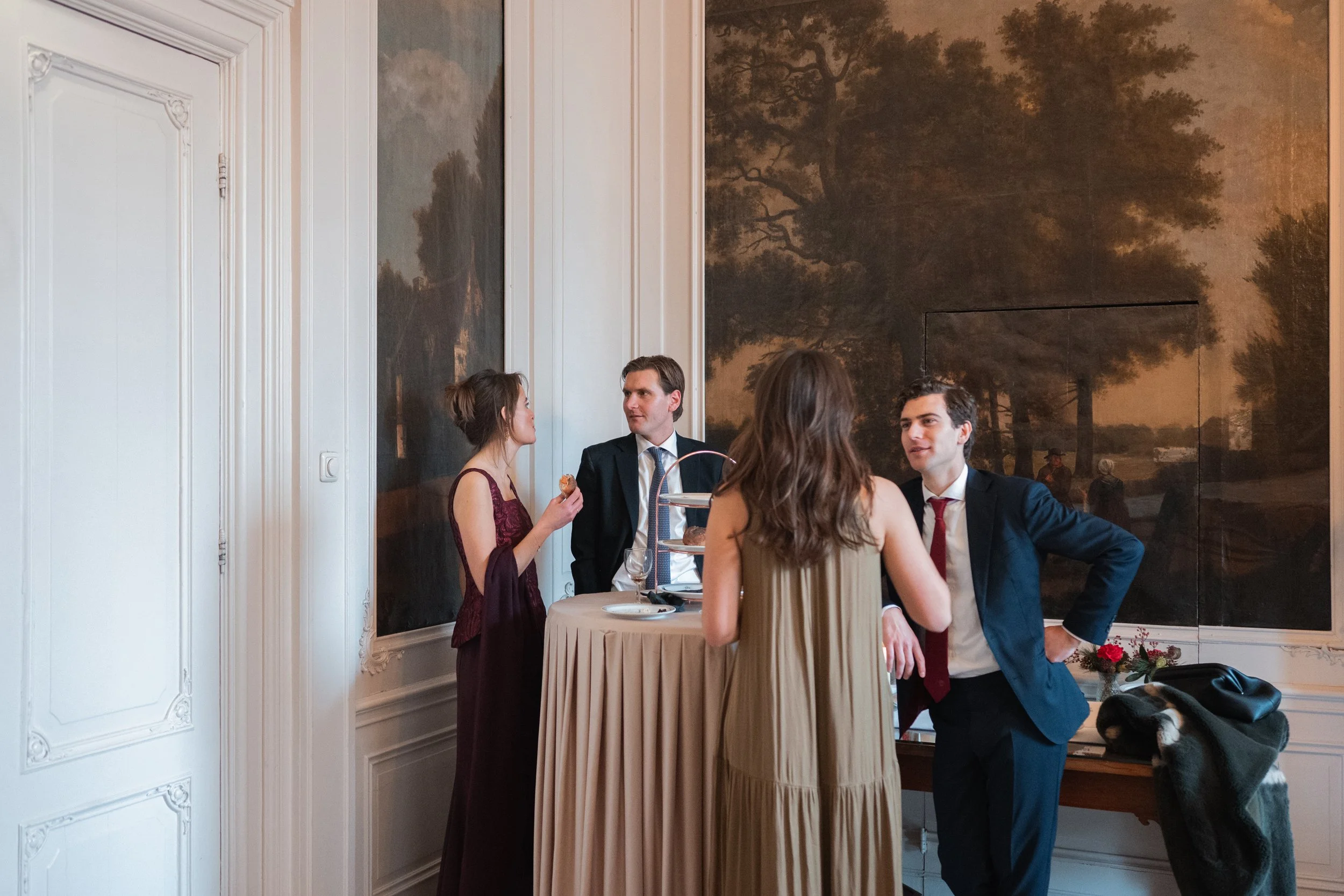 Four people dressed in formal attire are standing around a high table, engaging in conversation at an elegant indoor event.