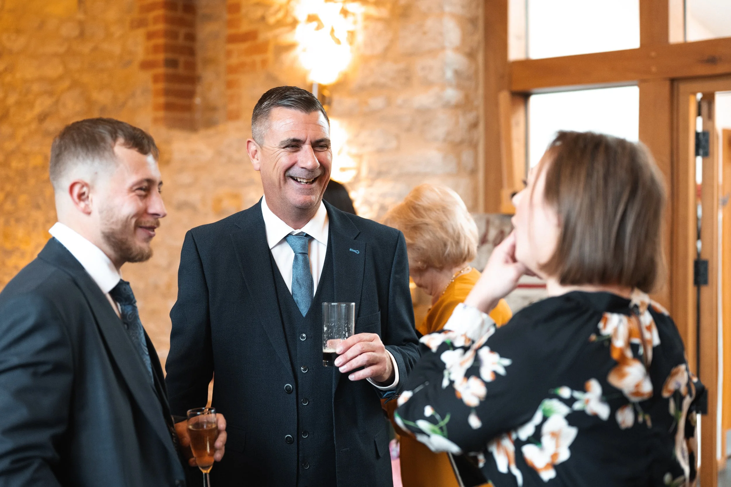 Group of middle-aged people at a social gathering, engaging in conversation and smiling, in a warmly lit brick-walled venue.
