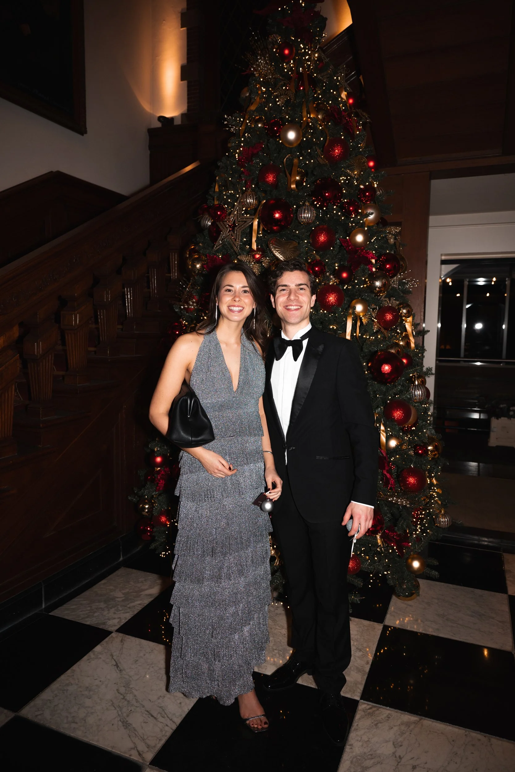 A couple dressed in formal wear standing in front of a decorated Christmas tree.