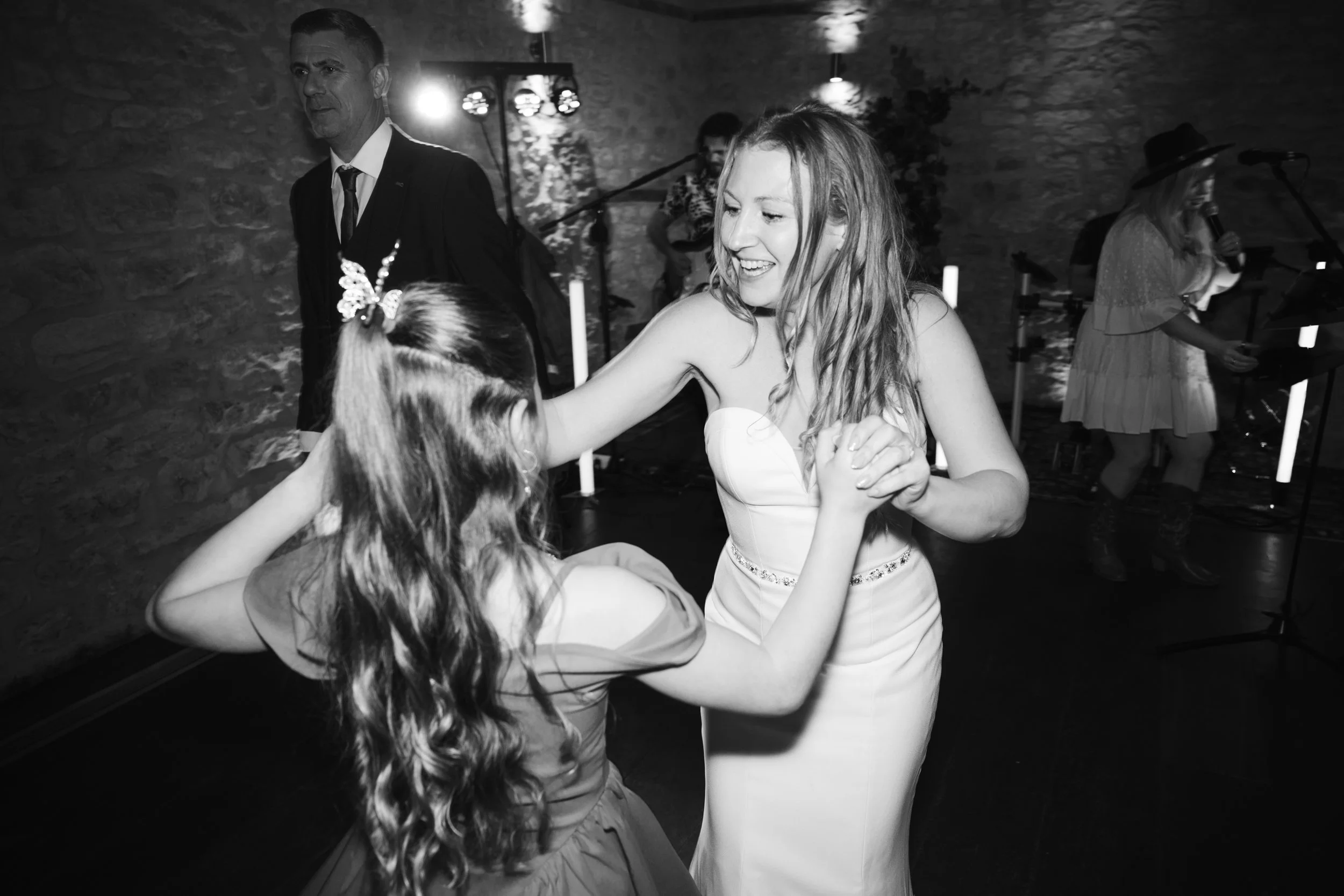 Two women dancing together at a celebration, with a band playing music in the background.