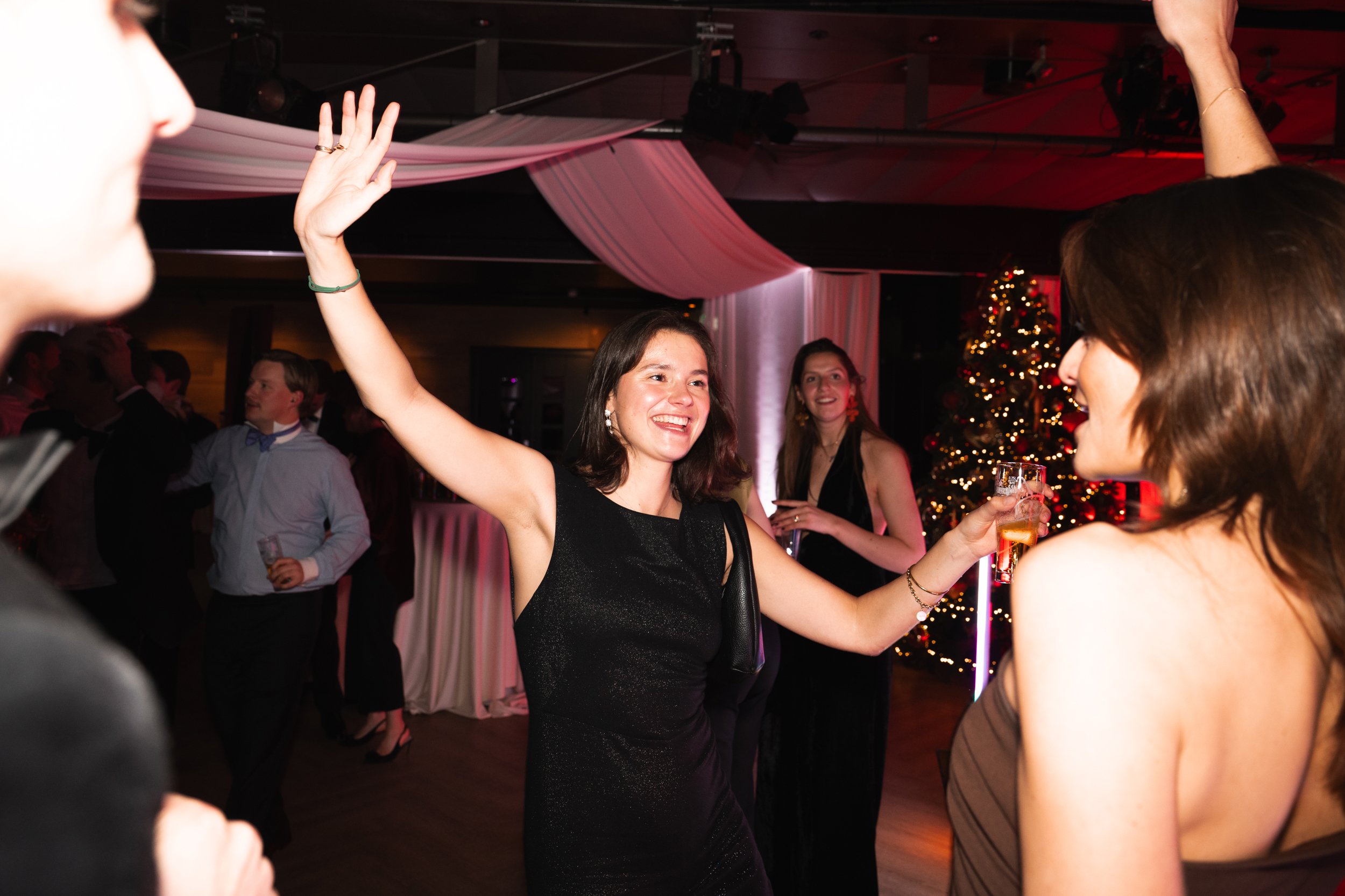 Women dancing and celebrating at a party with a decorated Christmas tree in the background.
