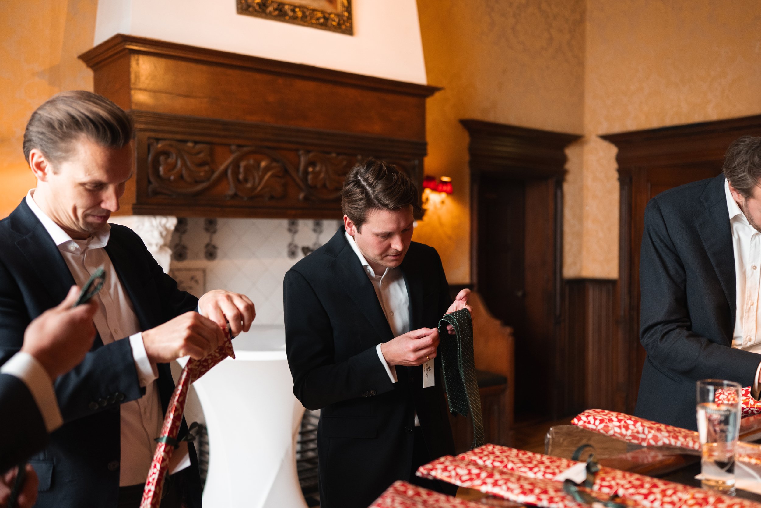 Men in formal attire wrapping Christmas presents at a table.