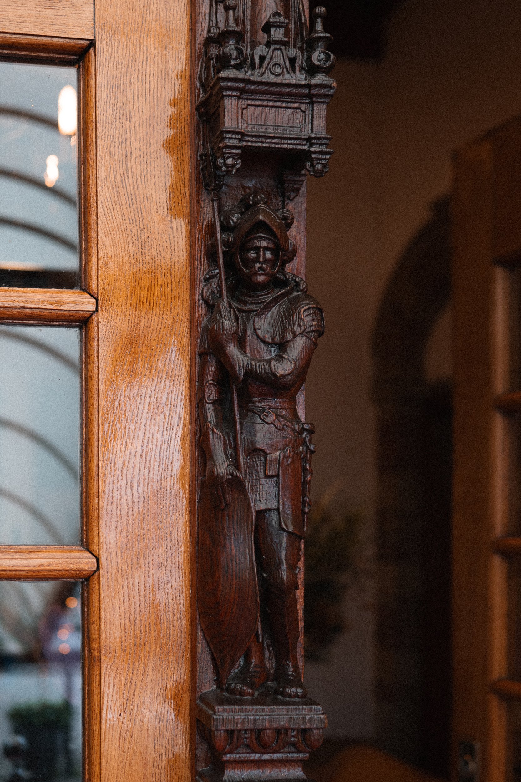 Wooden carved figure of a soldier dressed in armor, holding a staff, attached to a wooden frame or door, with some decorative elements above the figure.
