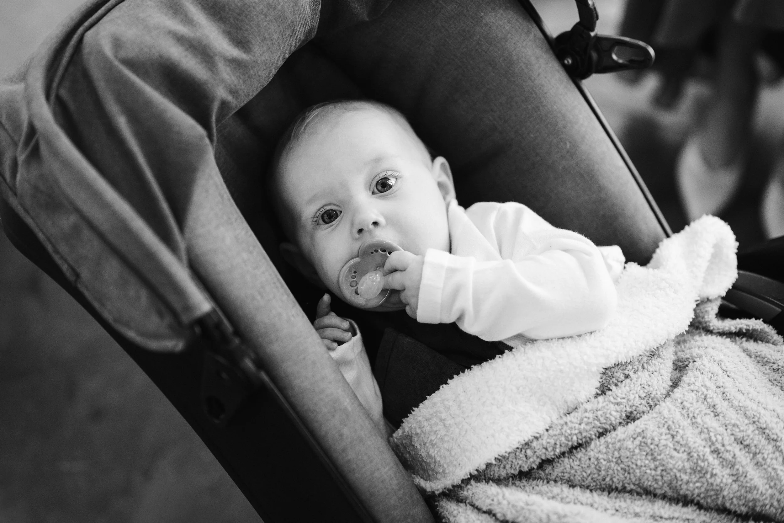 A baby with a pacifier lying in a stroller, looking at the camera.