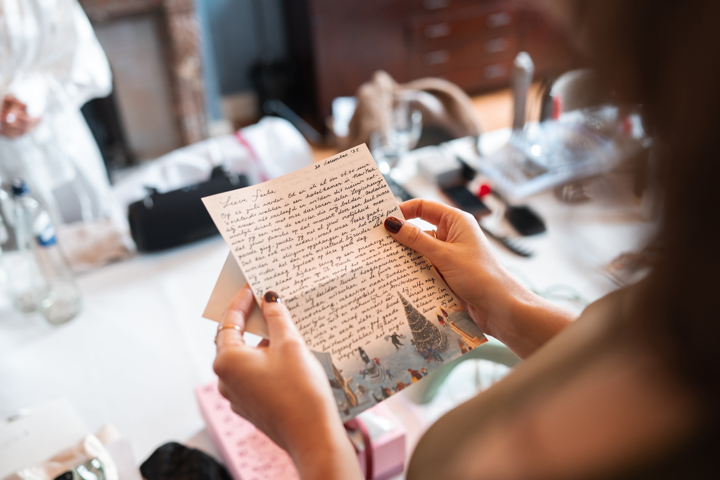 A woman holding a handwritten letter or card, with a cluttered table in the background.